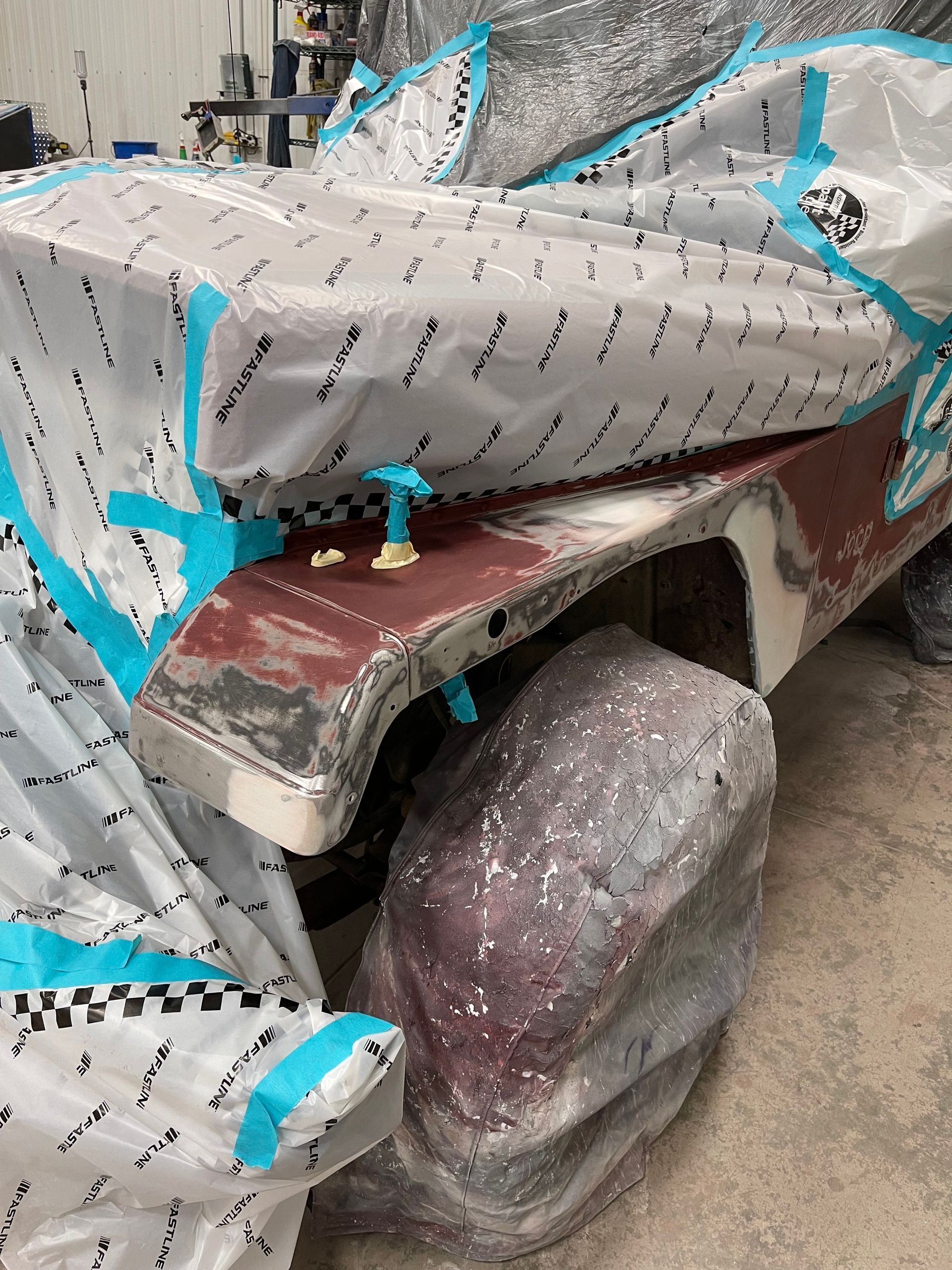 A car is covered in plastic wrap and tape in a garage.