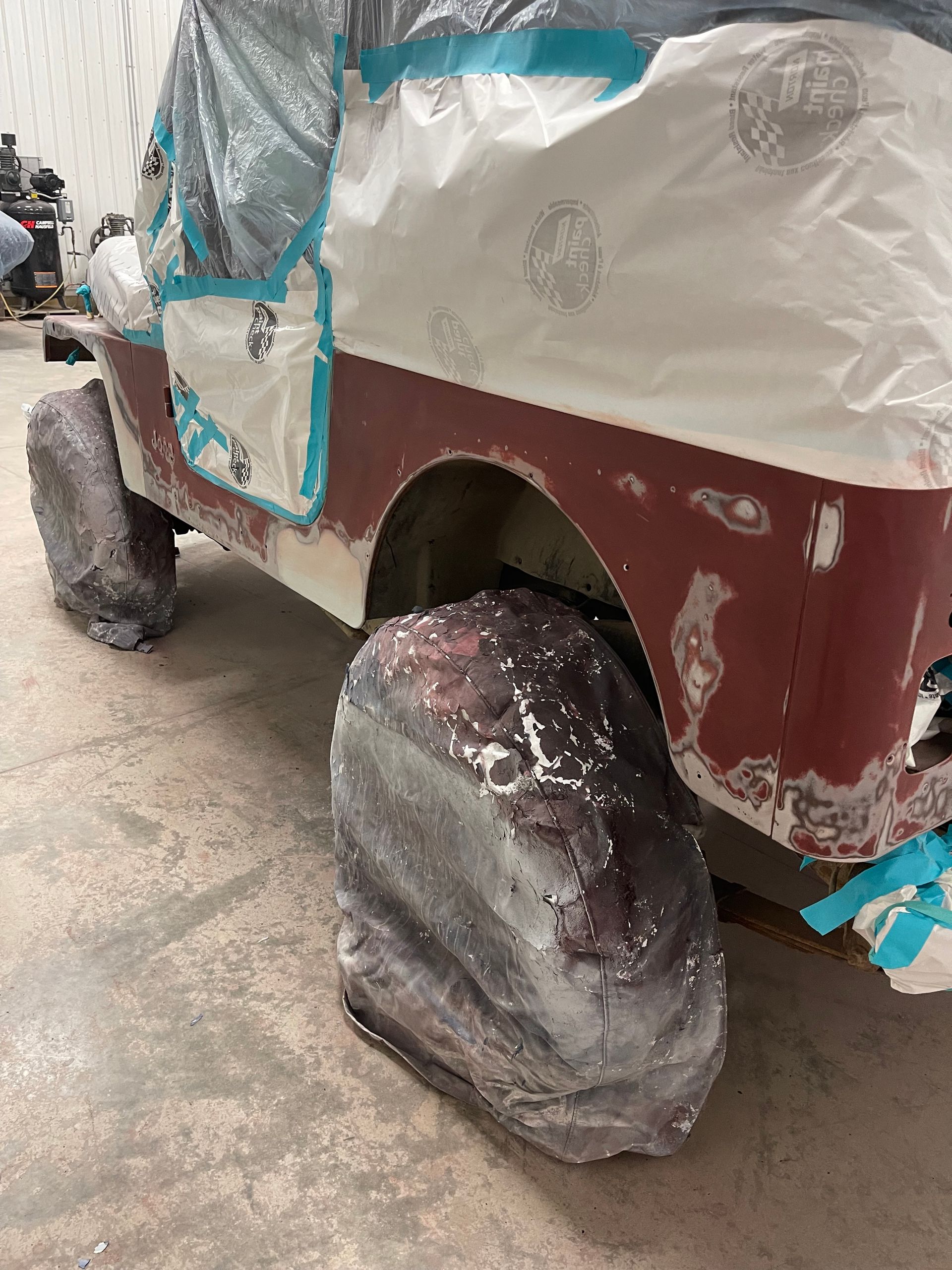 A jeep is covered in plastic wrap and is being painted.