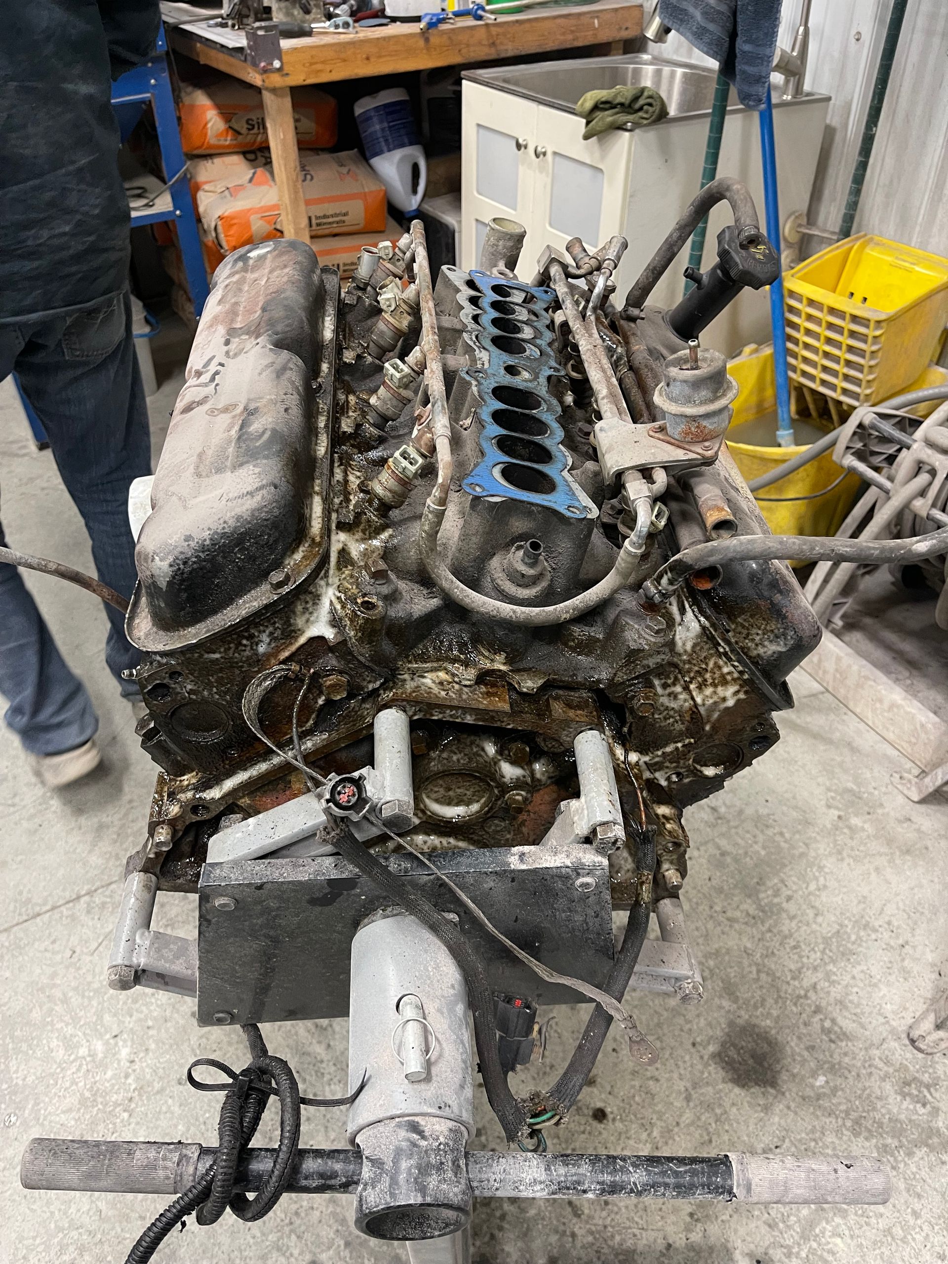 A dirty engine is sitting on a table in a garage.