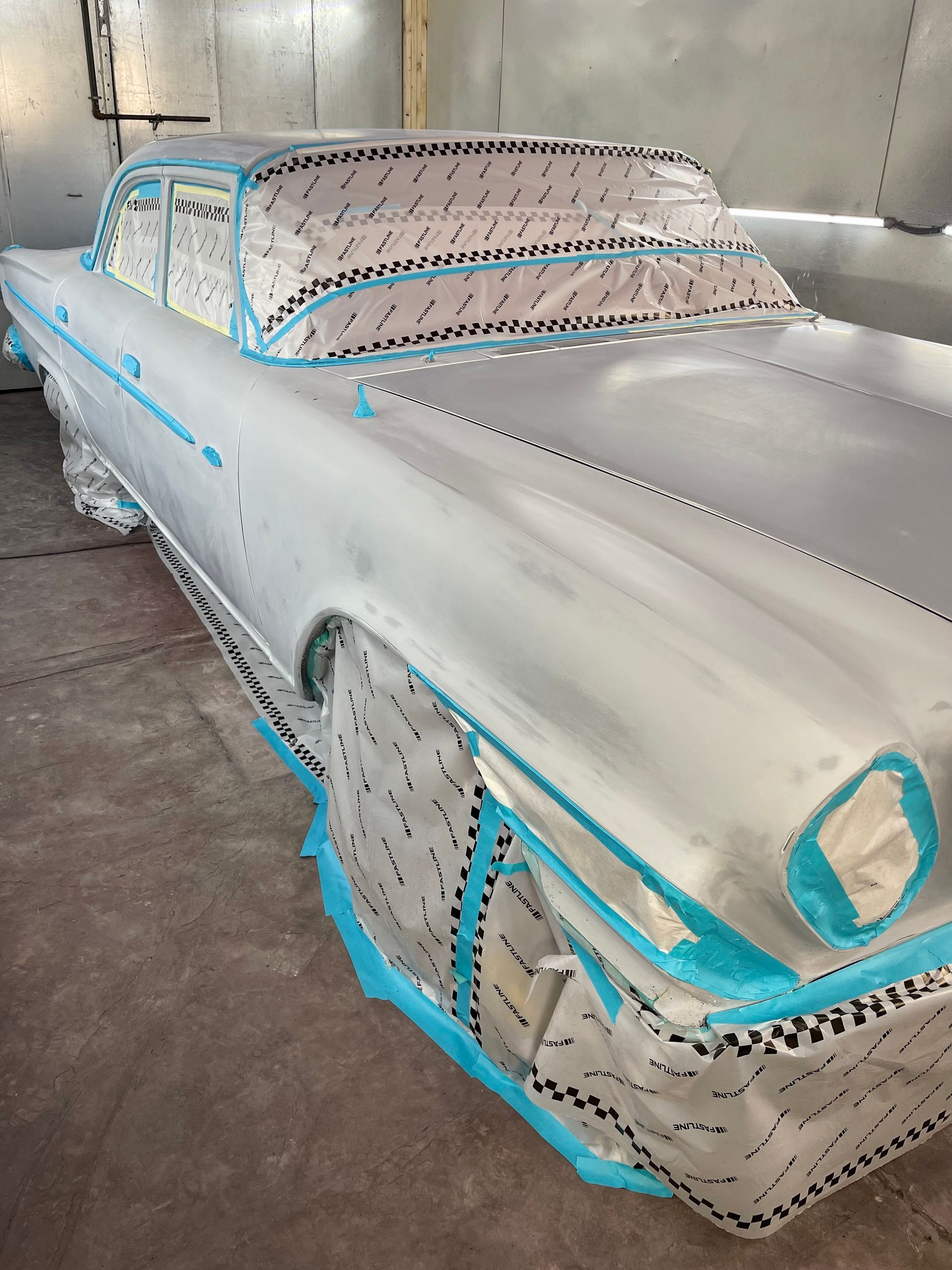 A silver car is being painted in a paint booth