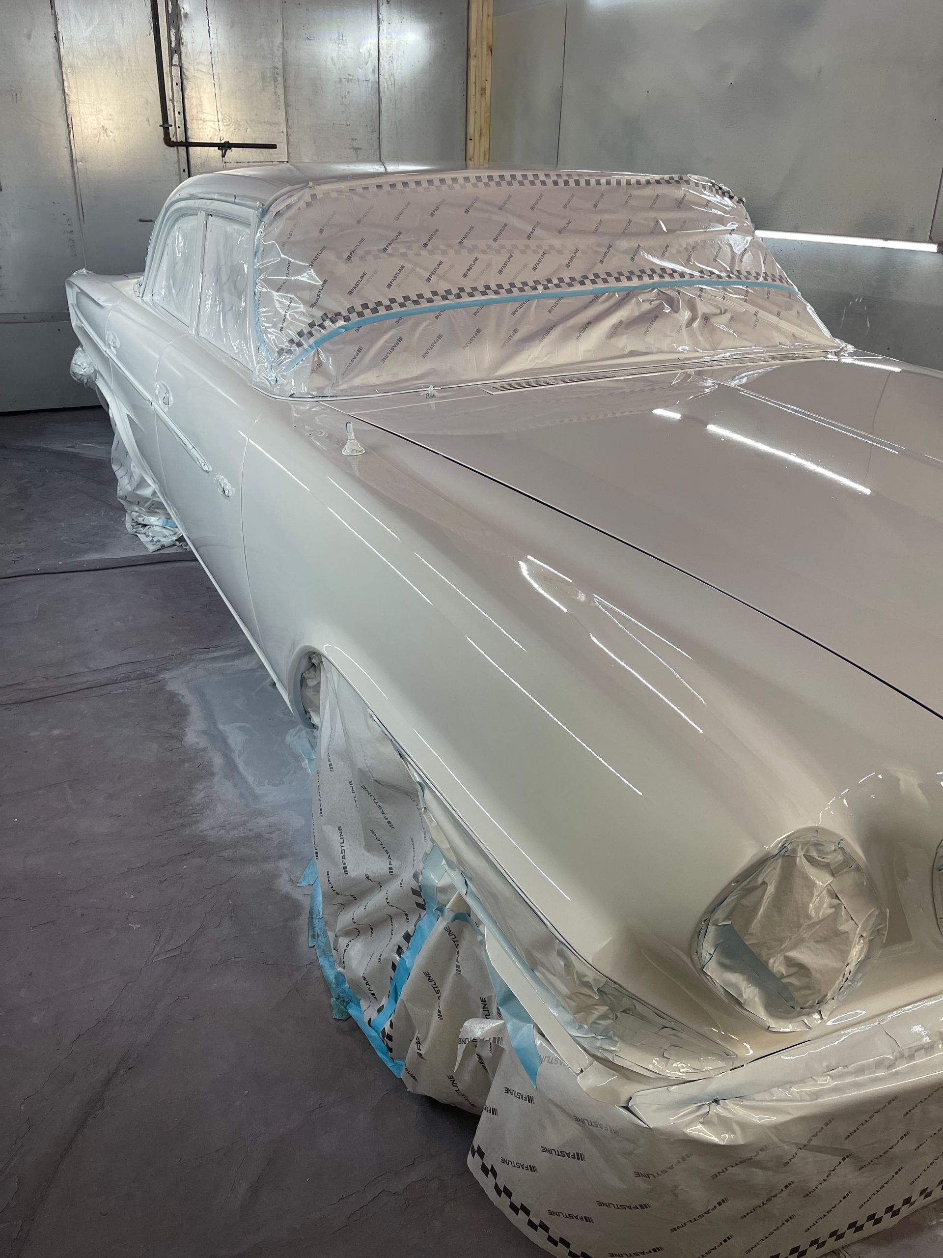 A white car is being painted in a paint booth