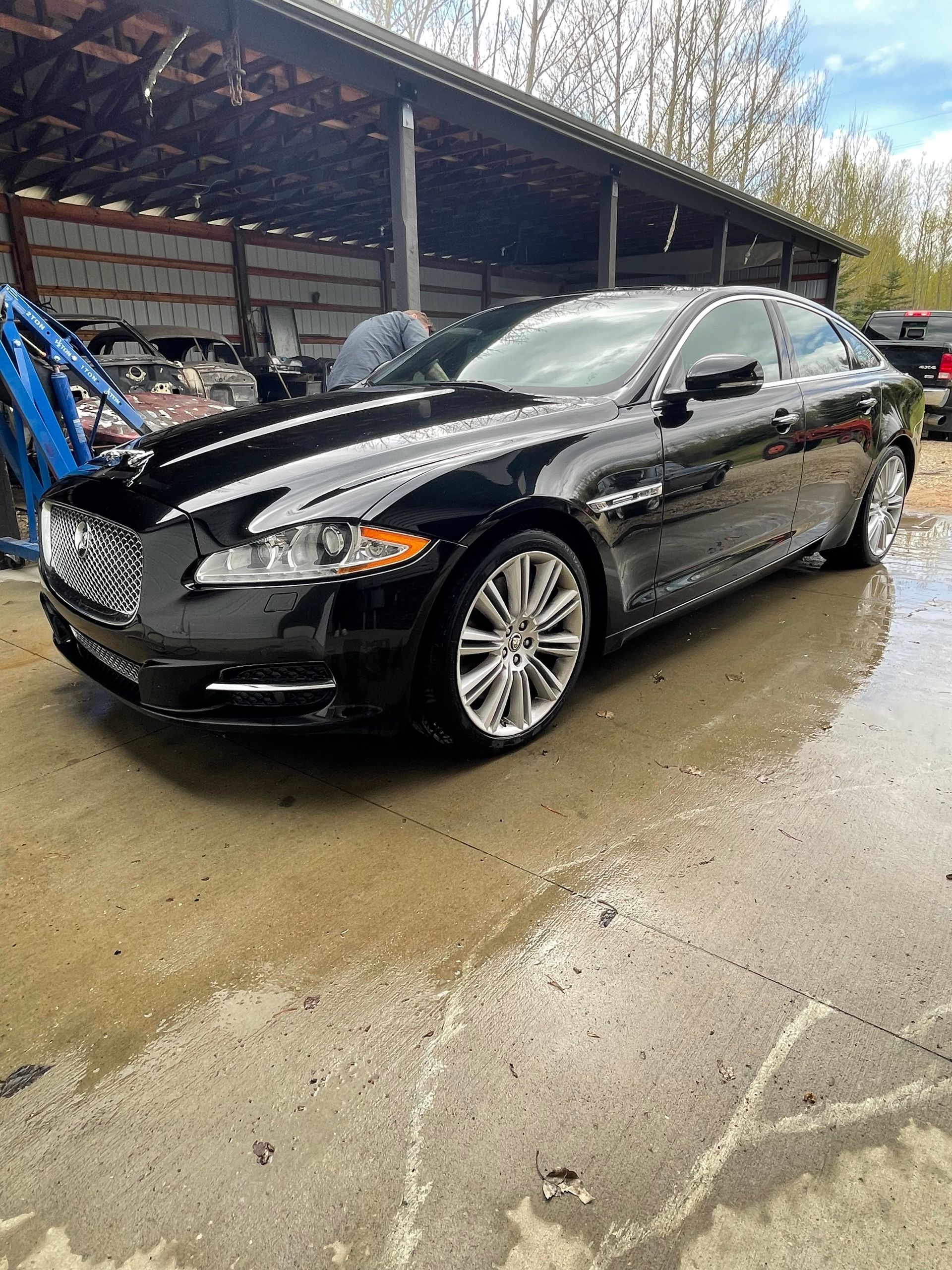 A black jaguar x type is parked in front of a shed.