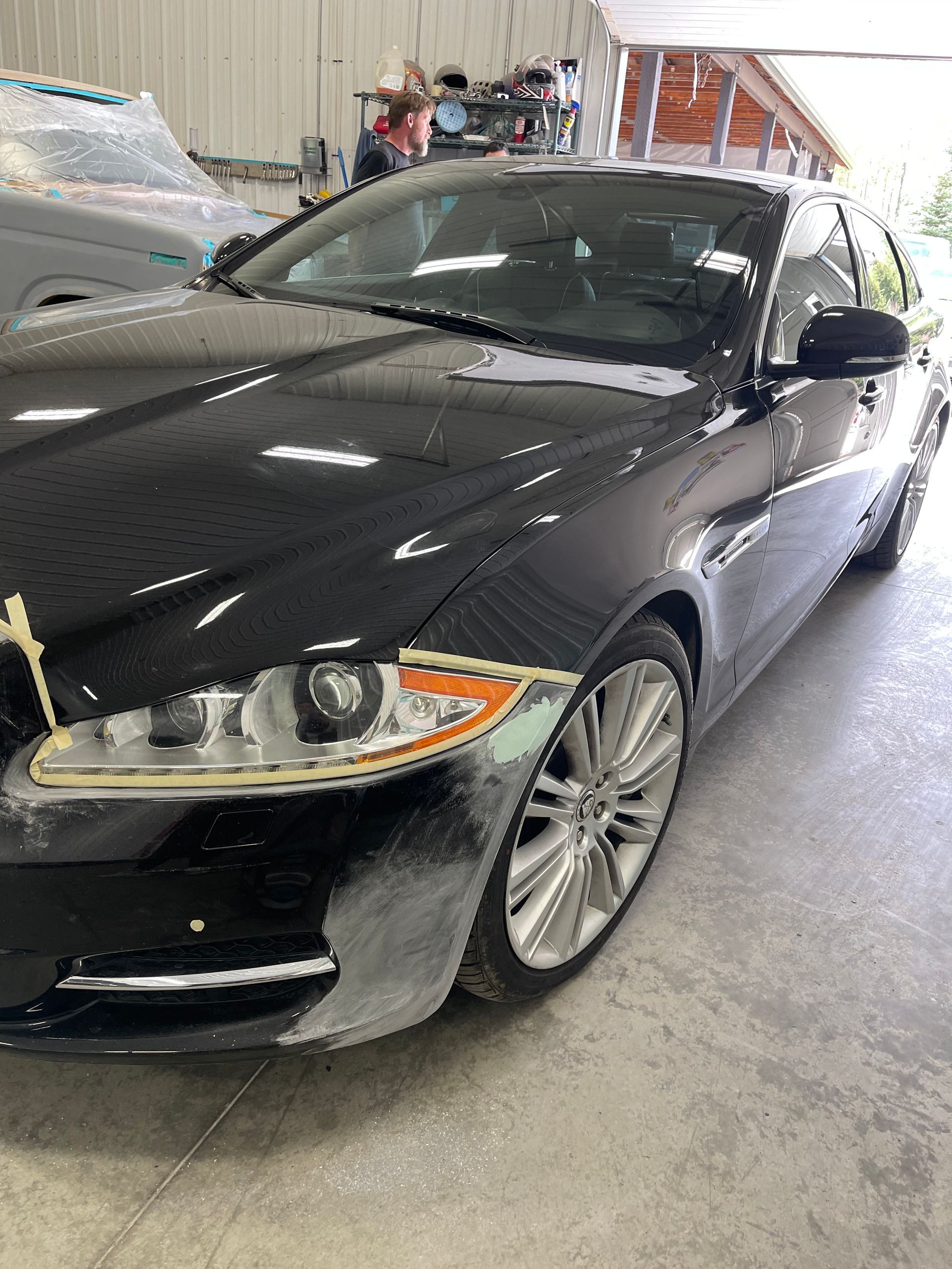 A black car with a damaged front bumper is parked in a garage.