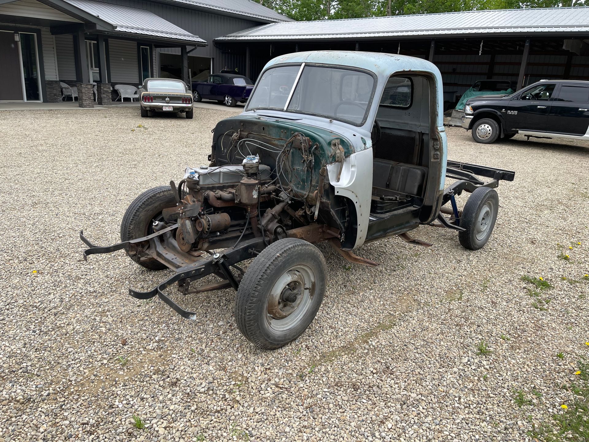 An old truck is sitting in a gravel lot in front of a building.