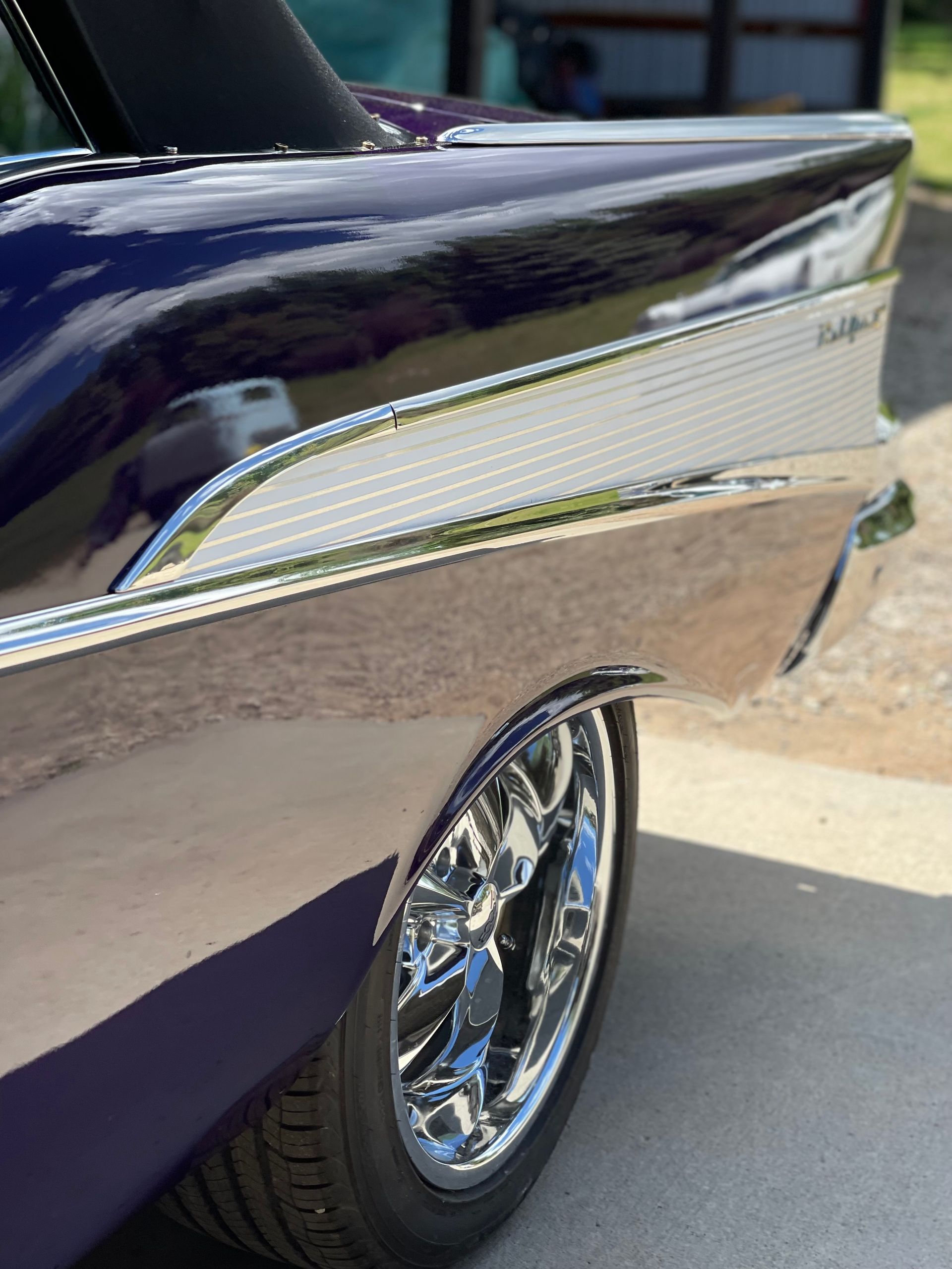 A purple car with chrome wheels is parked in a driveway.