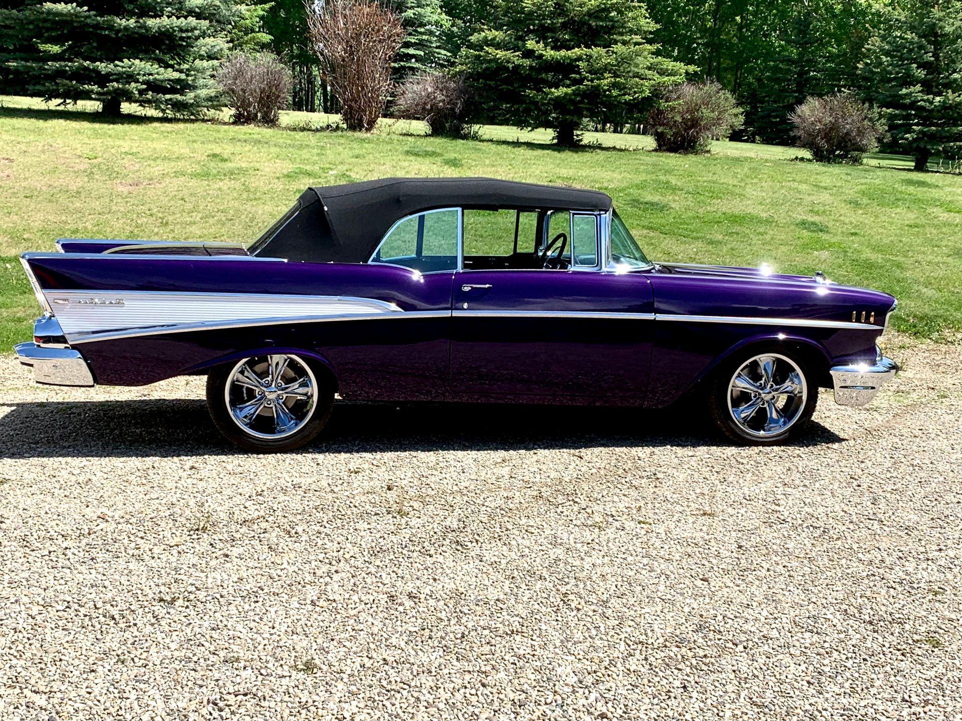 A purple convertible car is parked in a gravel lot.