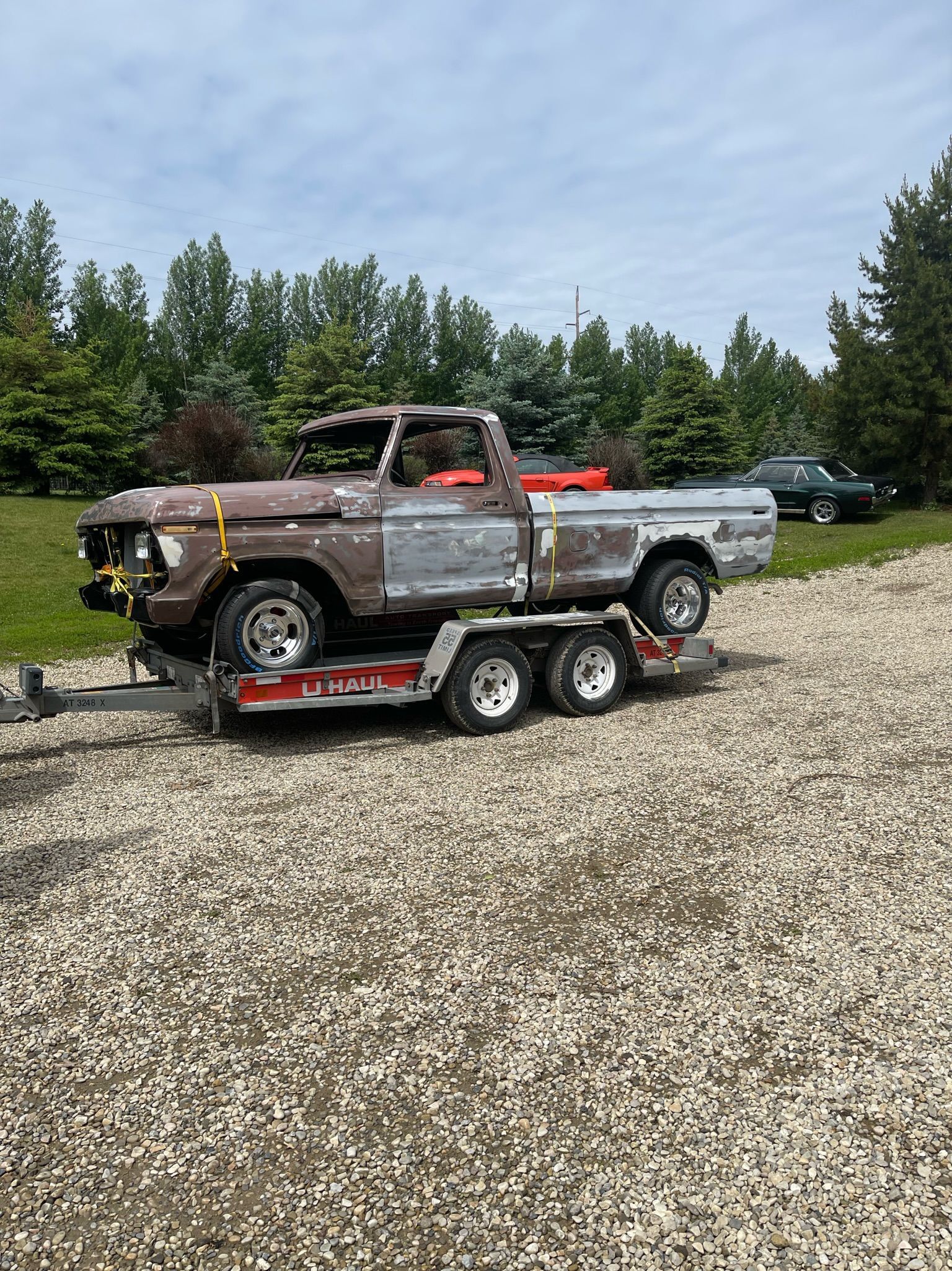 A truck is sitting on top of a trailer in a gravel lot.