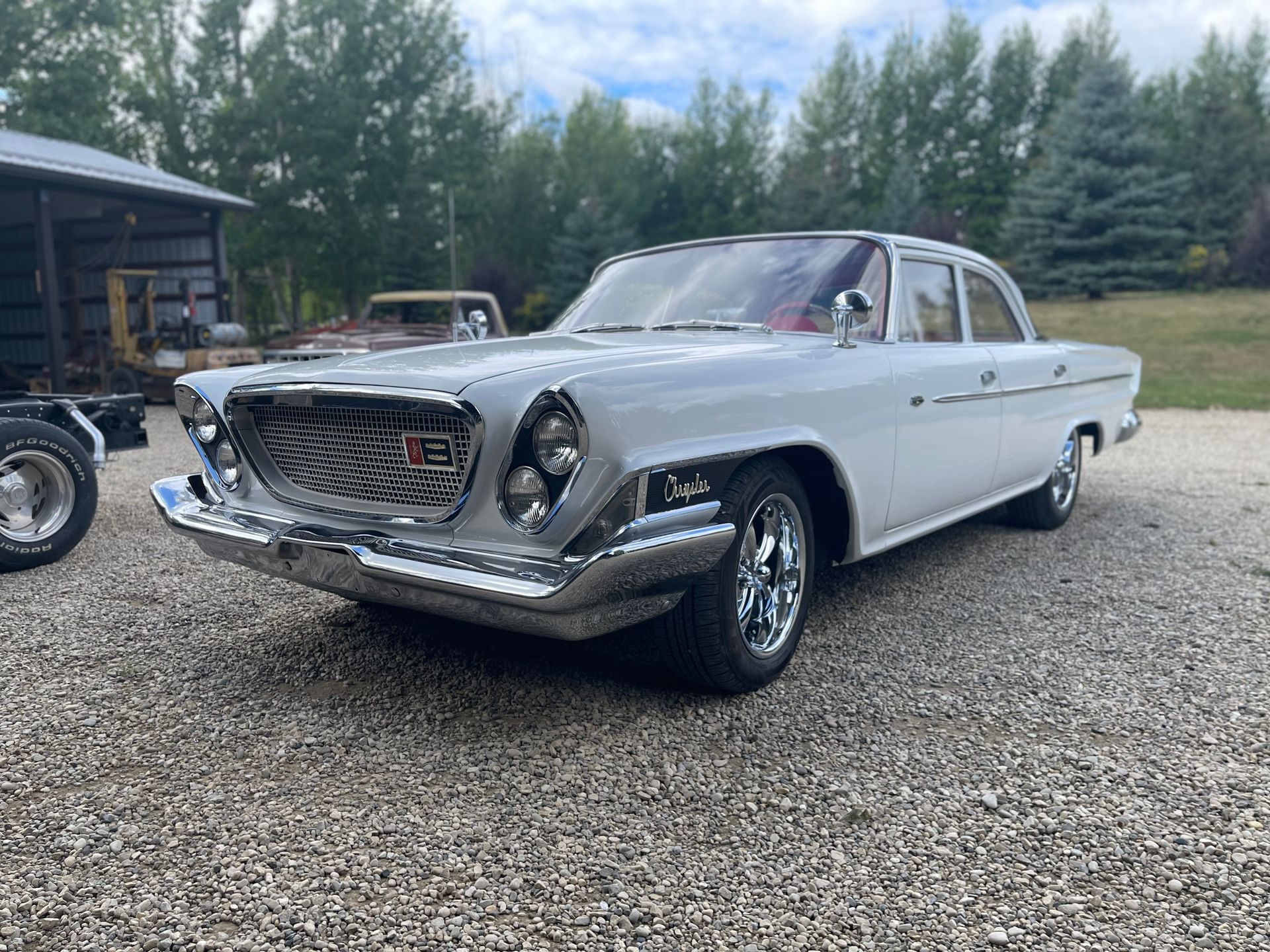 A white car is parked in a gravel lot.