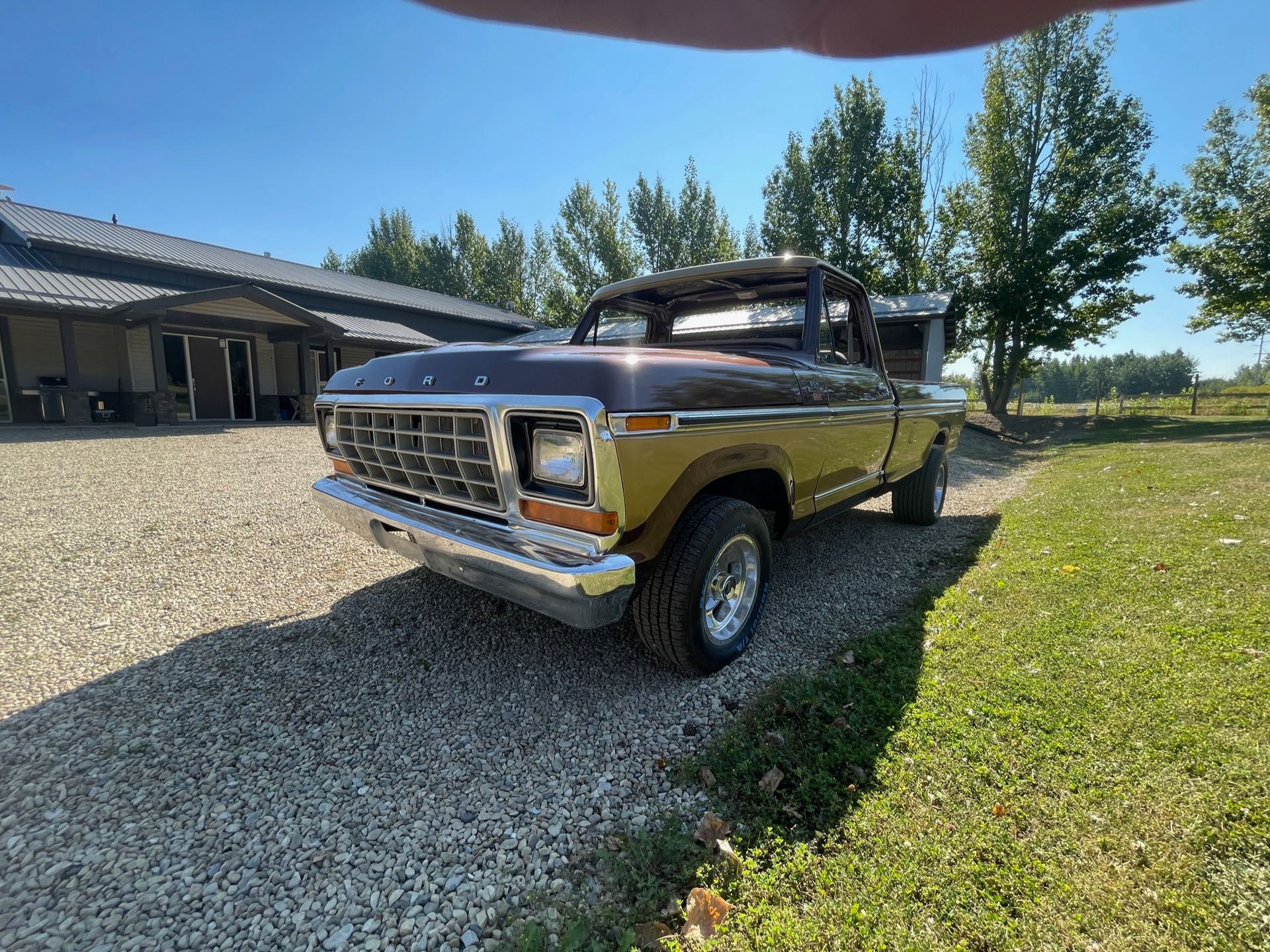 A ford truck is parked in a gravel driveway in front of a house.