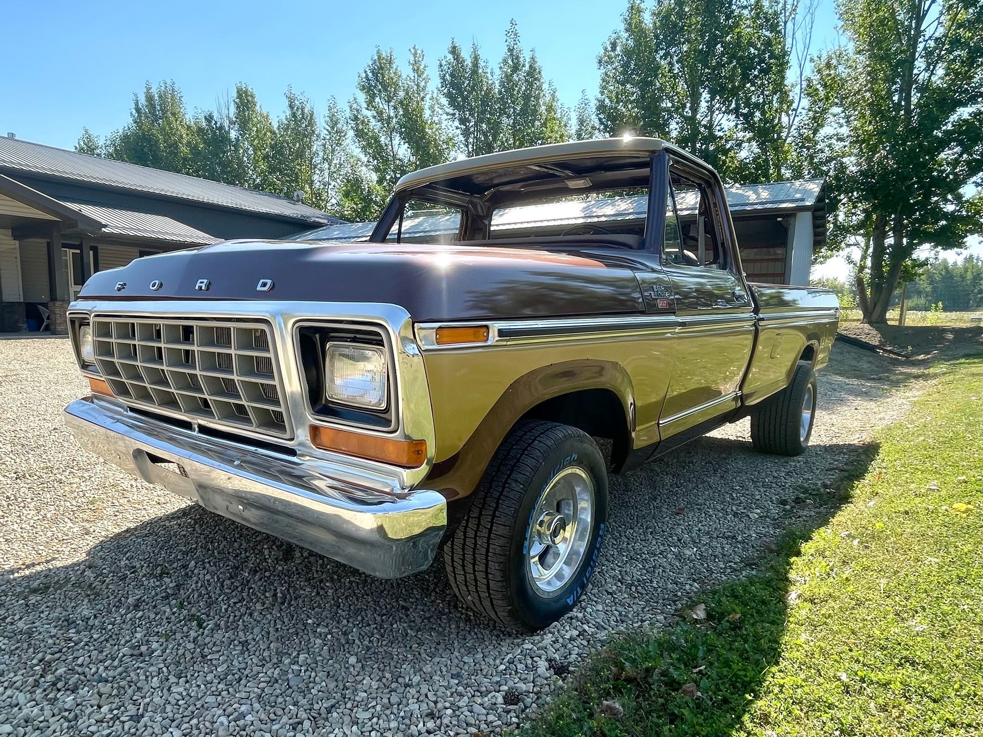 A brown ford truck is parked in a gravel driveway in front of a house.
