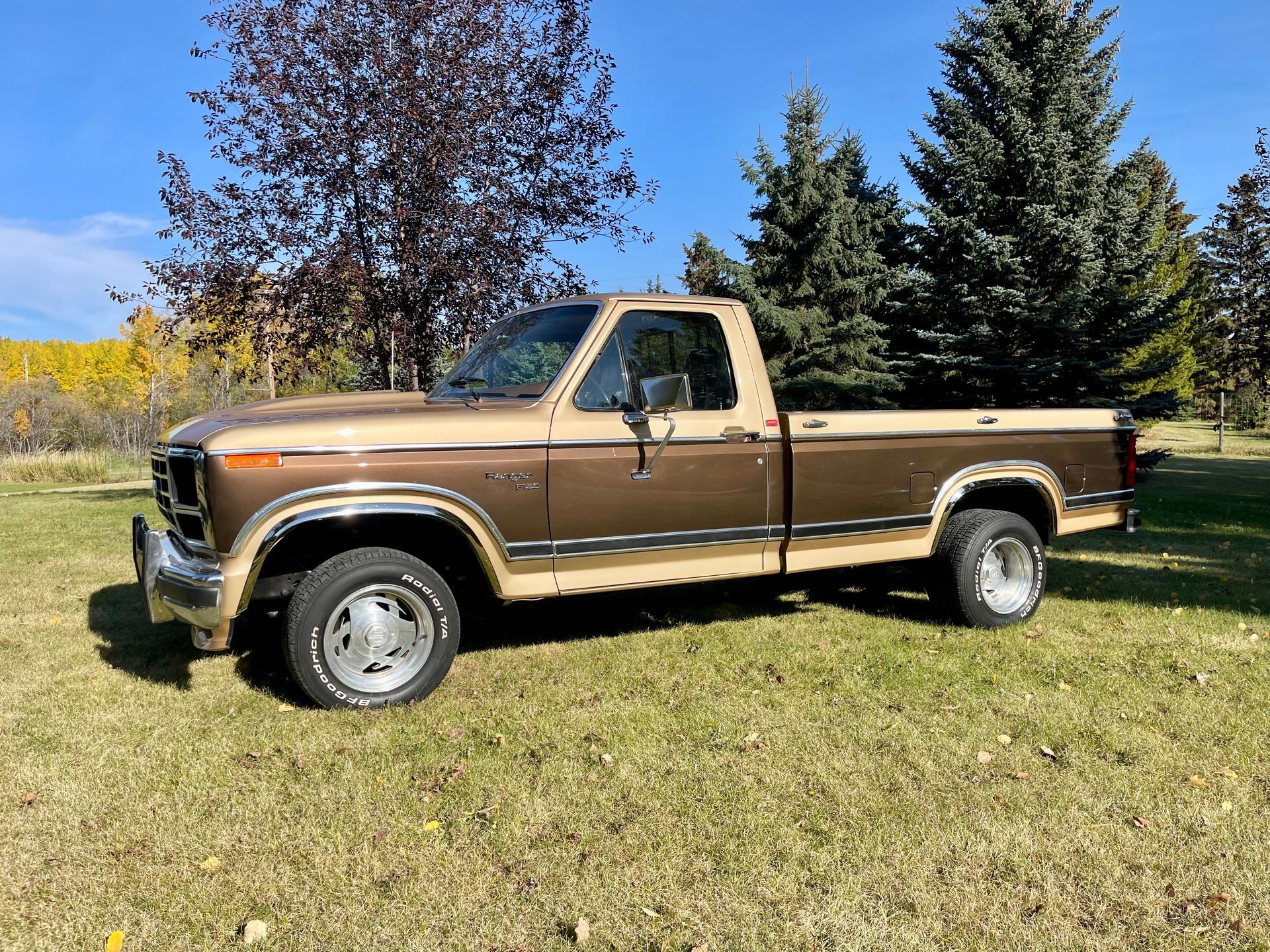 A brown and tan pickup truck is parked in a grassy field.