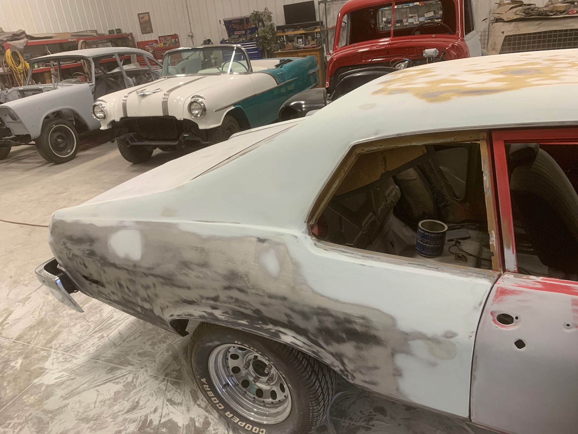 A white car is being painted in a garage with other cars.