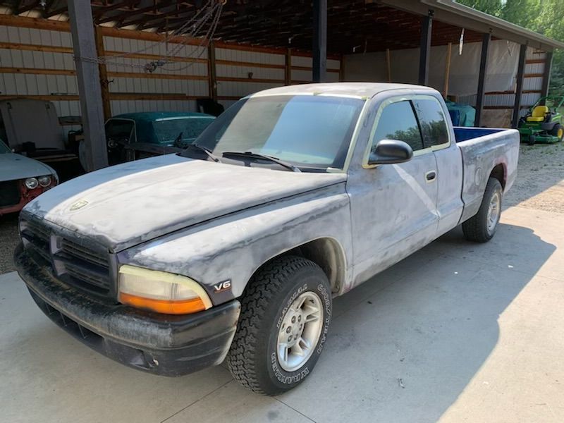 A gray truck is parked in front of a shed.