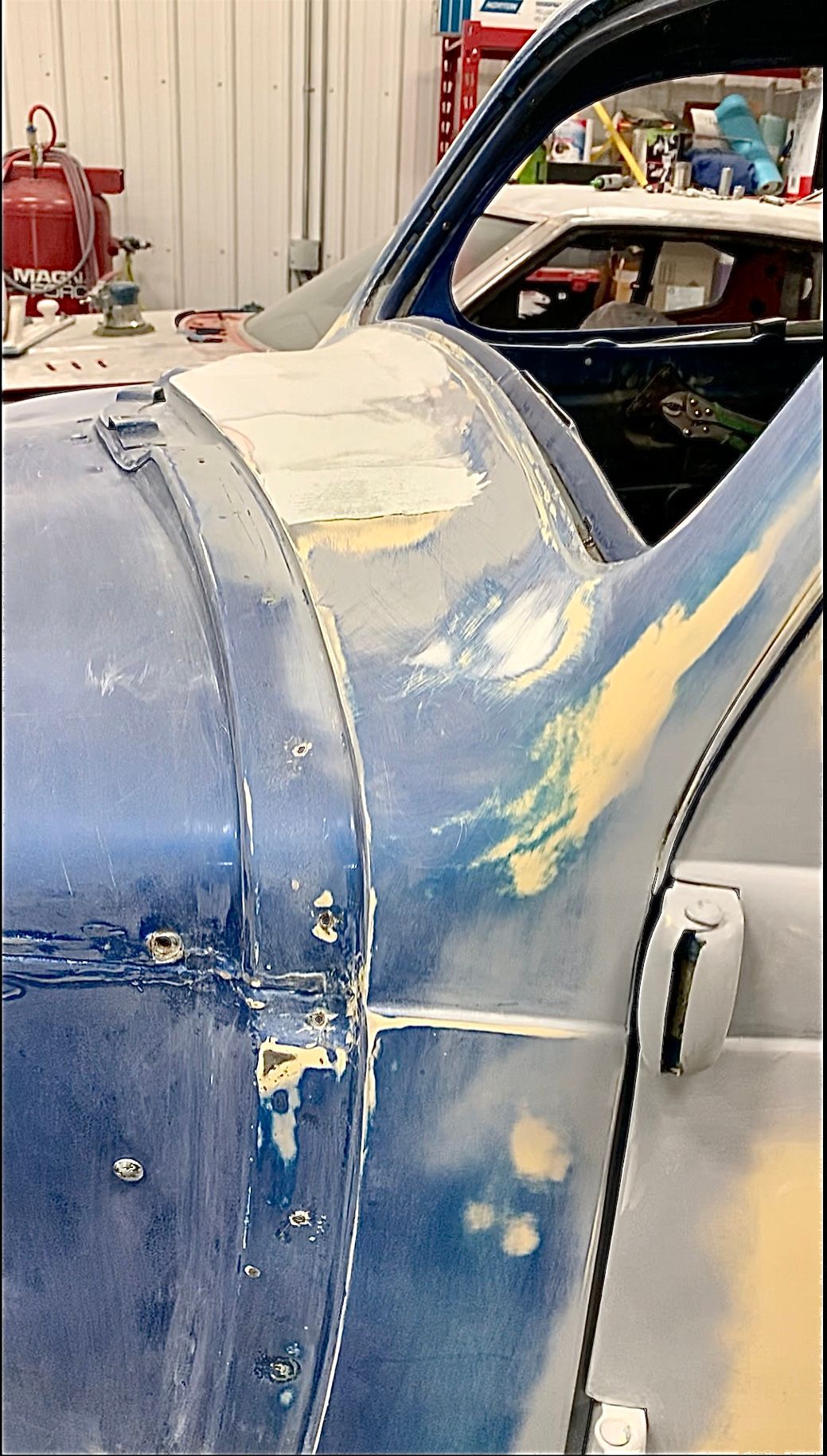 A blue car is being painted in a garage.