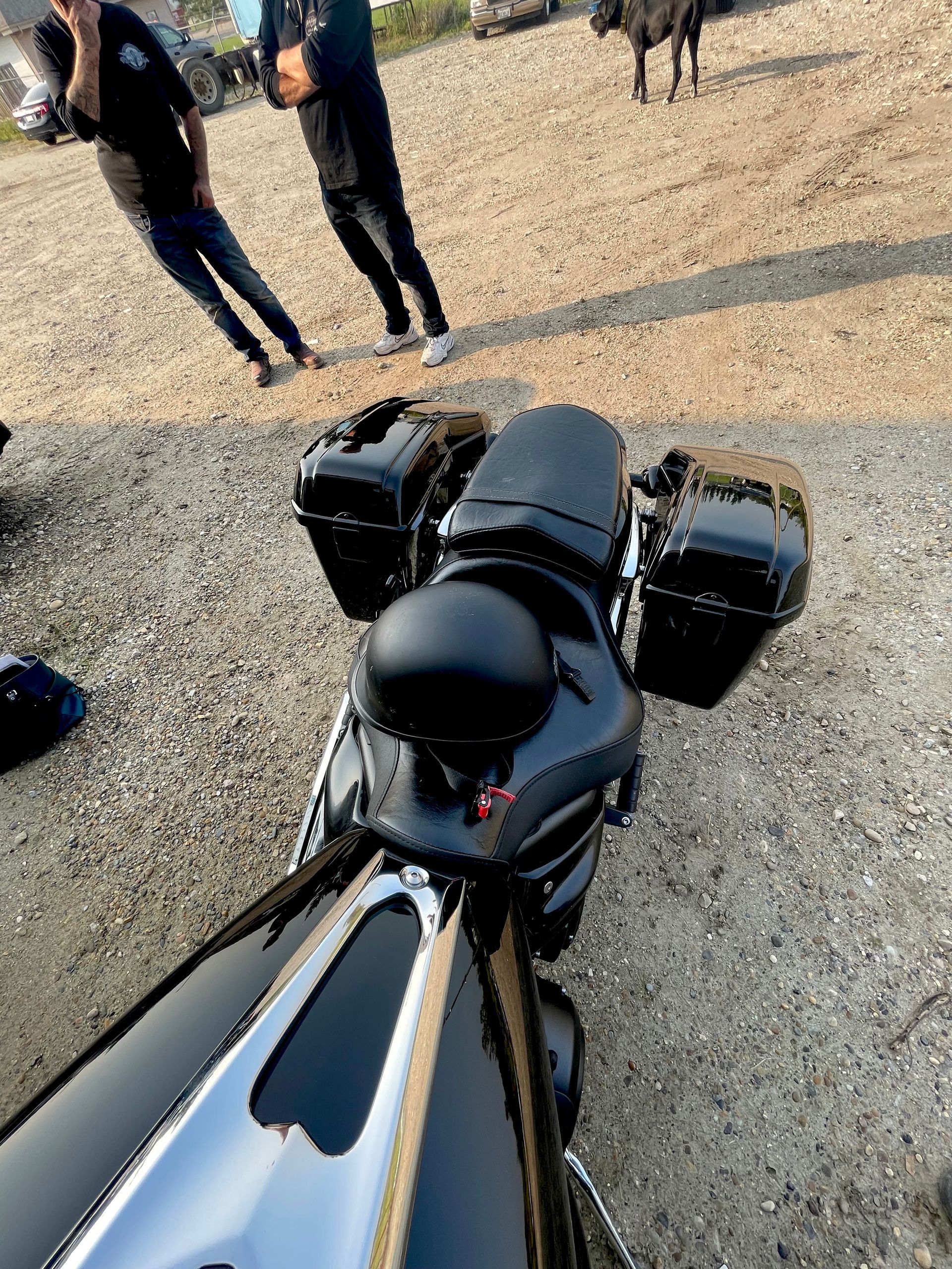 A motorcycle is parked in a gravel lot with people standing around it.