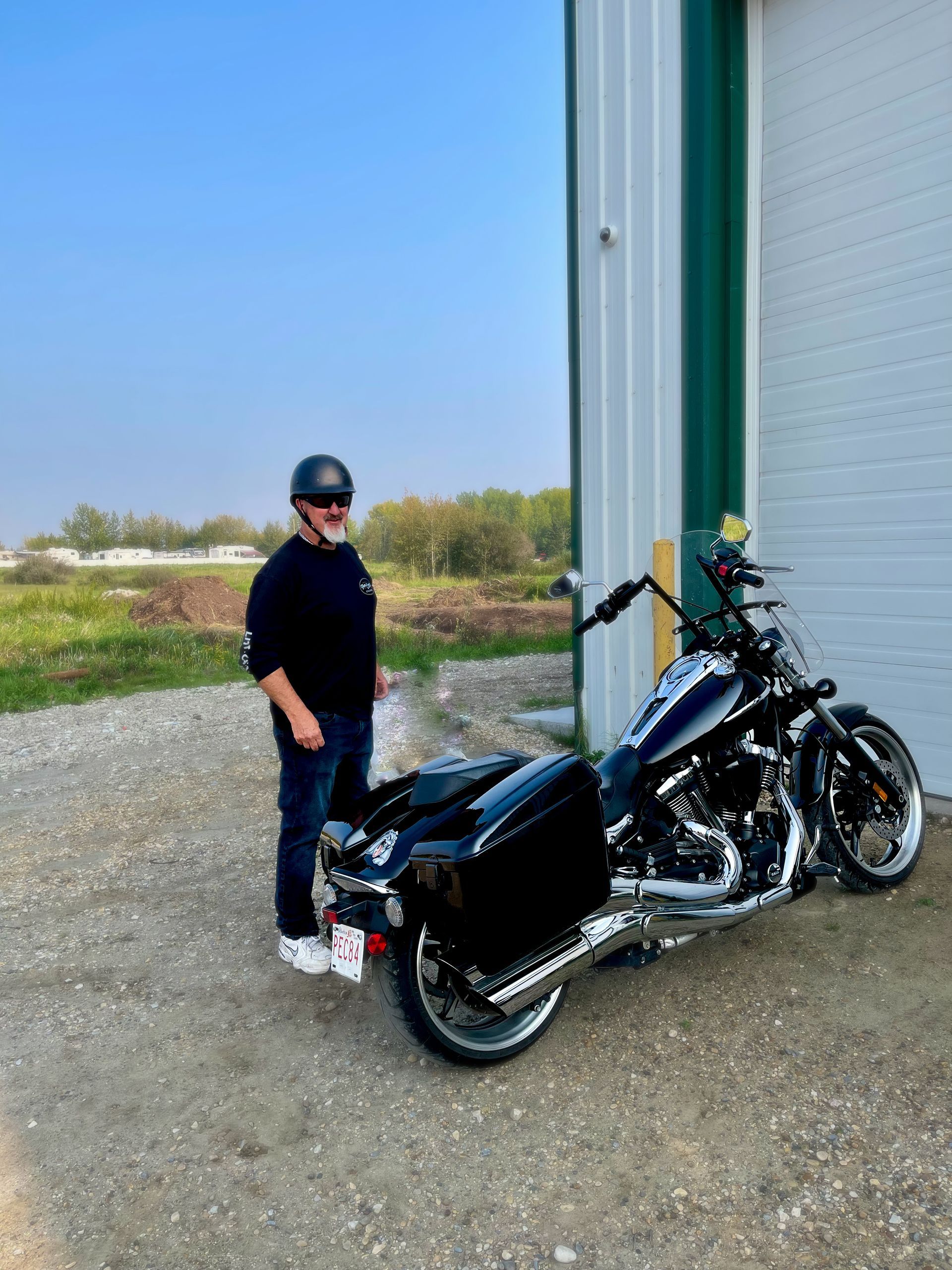 A man is standing next to a black motorcycle in front of a garage.