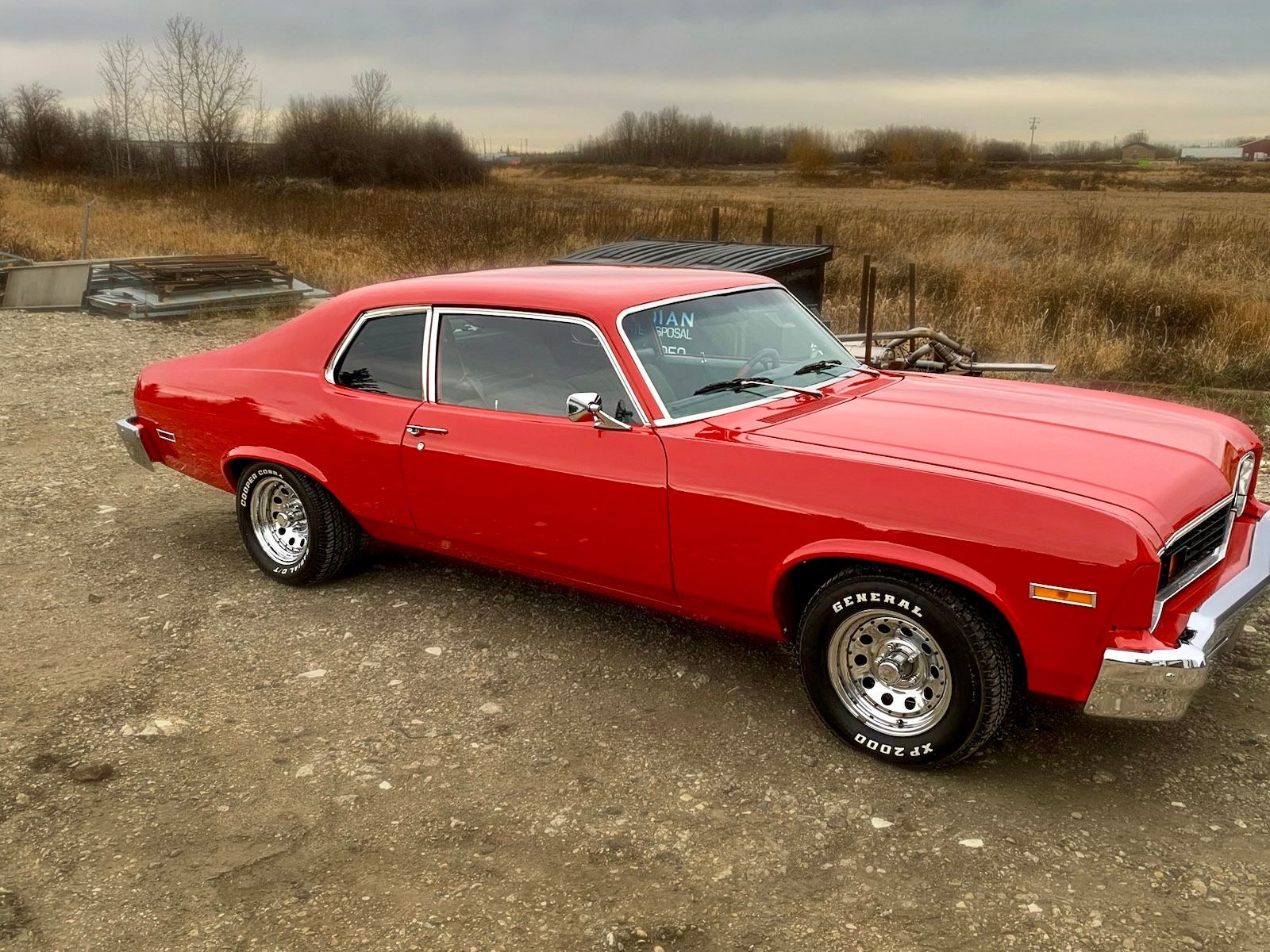 A red car is parked on a dirt road in a field.
