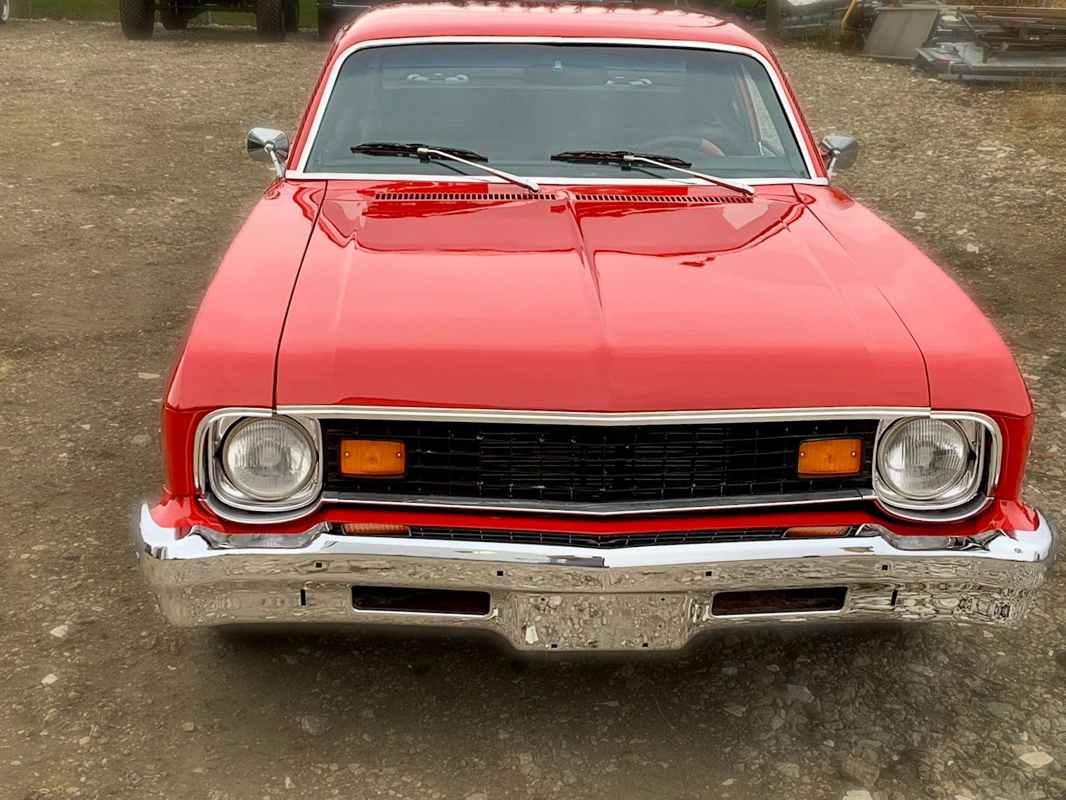 A red car is parked in a gravel lot.