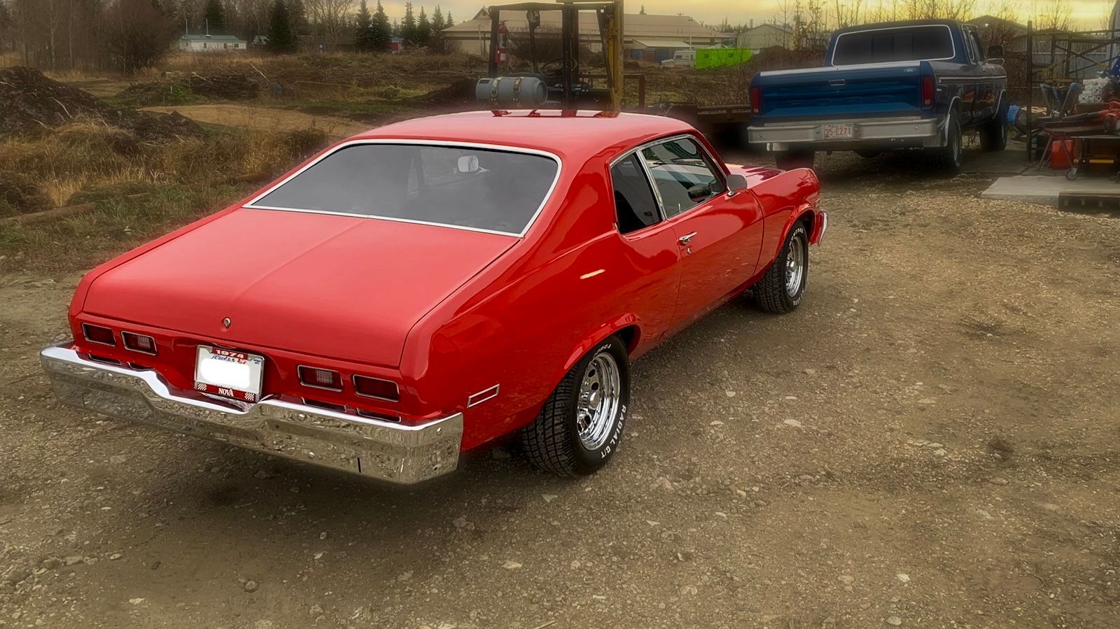 A red car is parked in a gravel lot next to a blue truck.