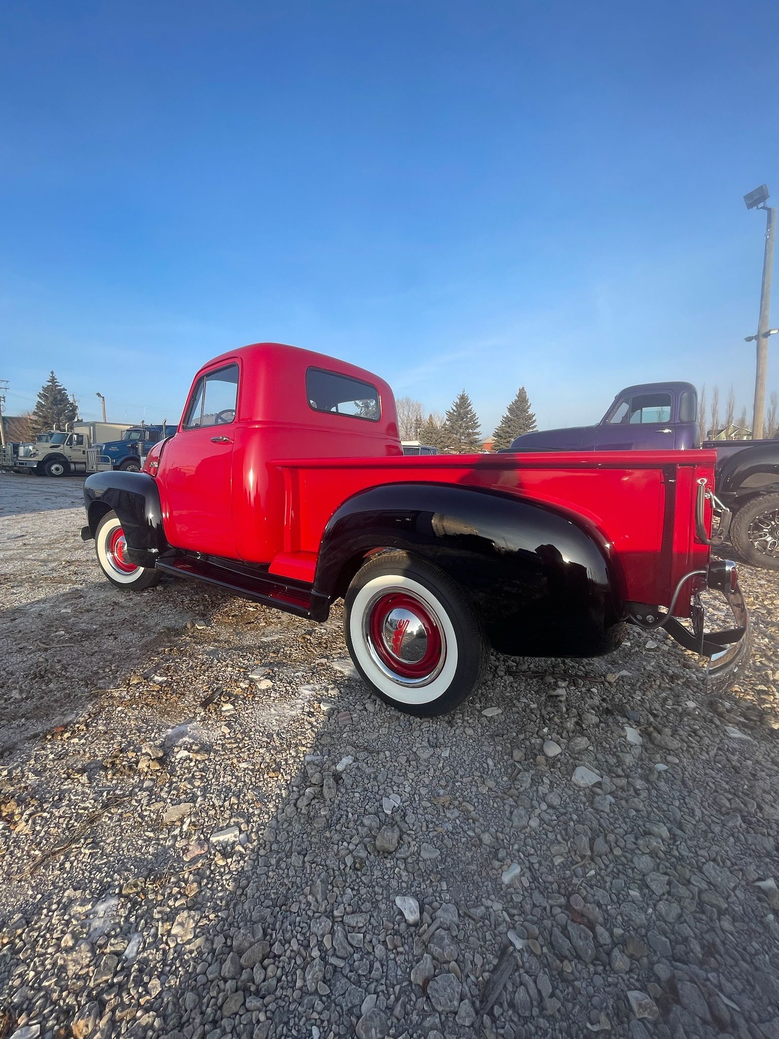 A red truck is parked in a gravel lot.