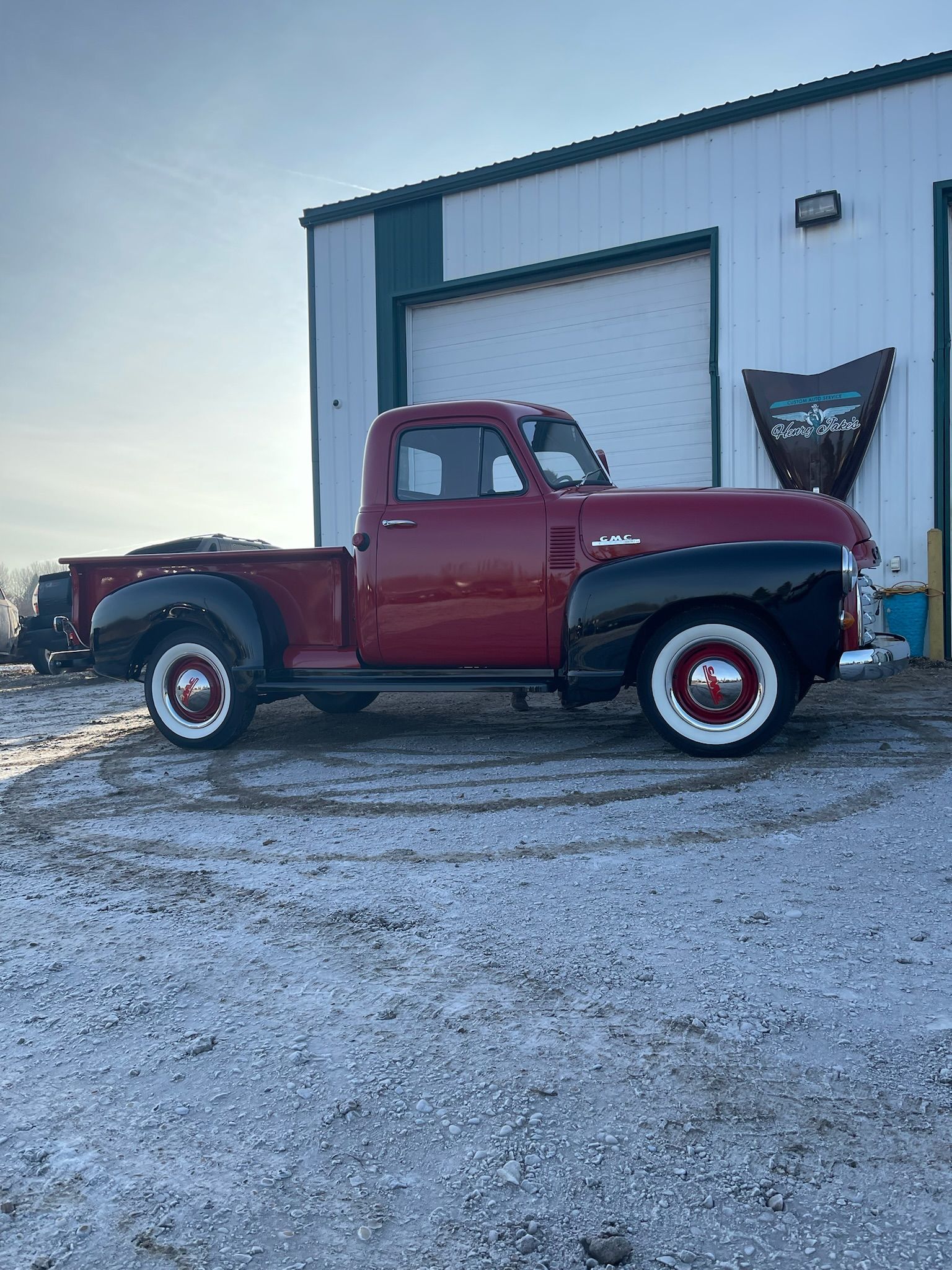 An old red truck is parked in front of a garage.