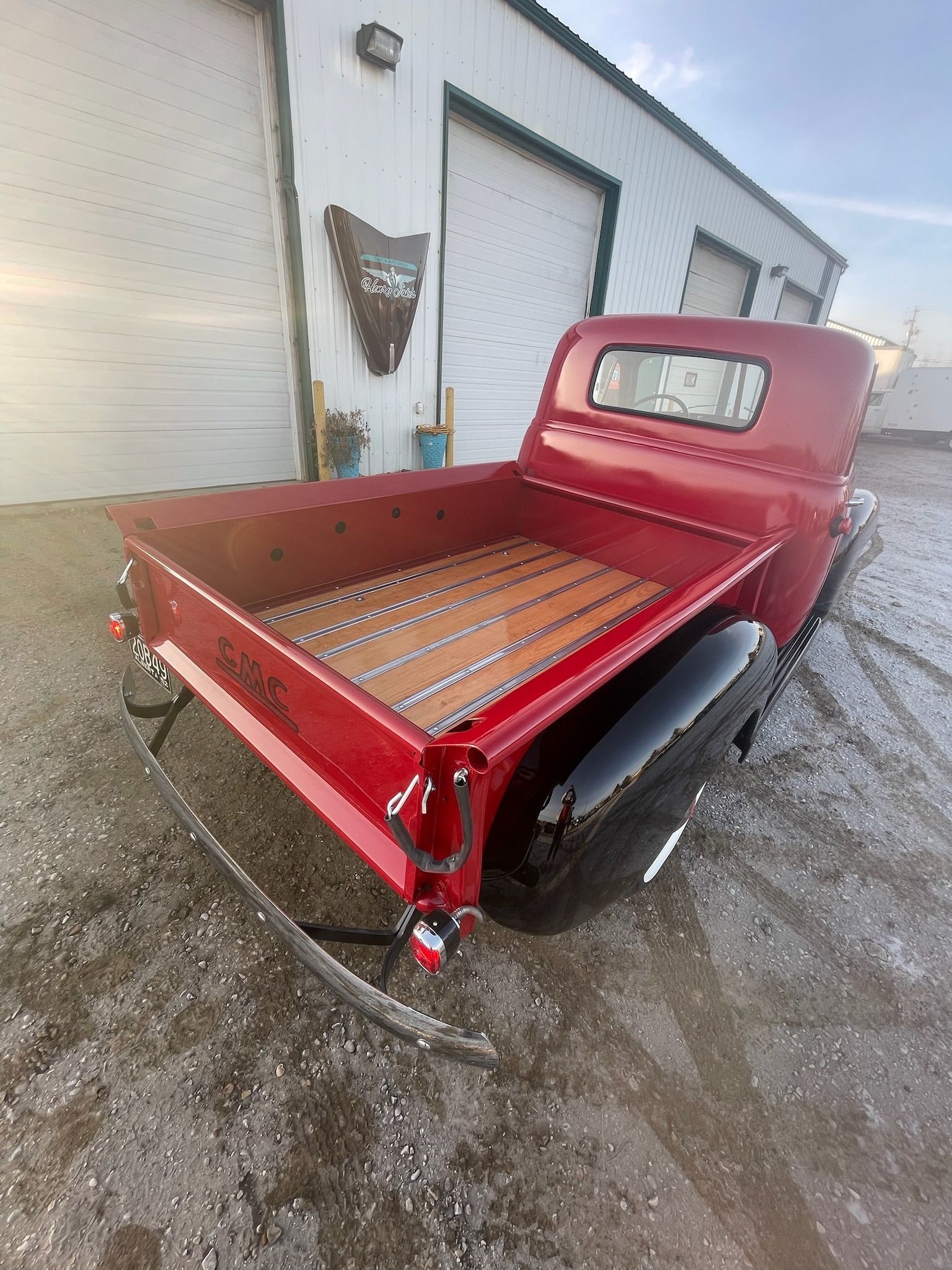 A red truck with a wooden bed is parked in front of a garage.