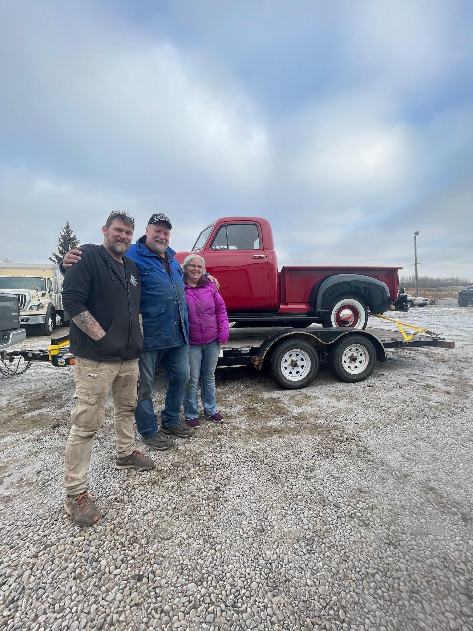 A group of people standing next to a red truck on a trailer.