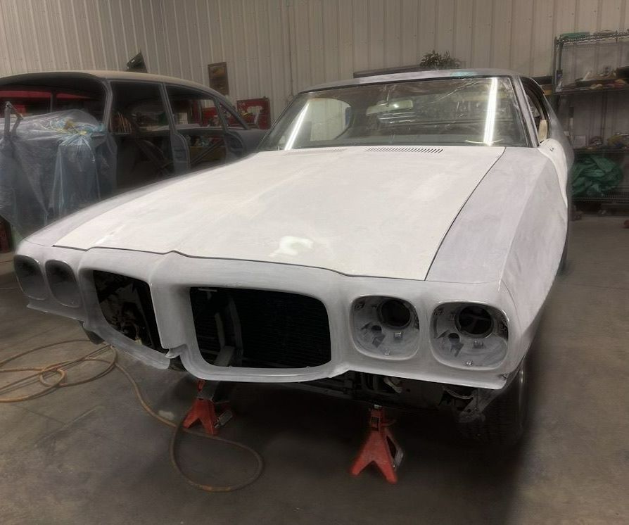 A white car is sitting on jack stands in a garage.