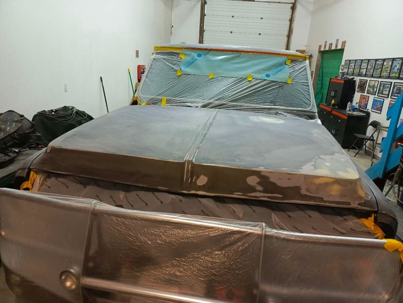 The hood of a truck is covered in plastic and is sitting in a garage.