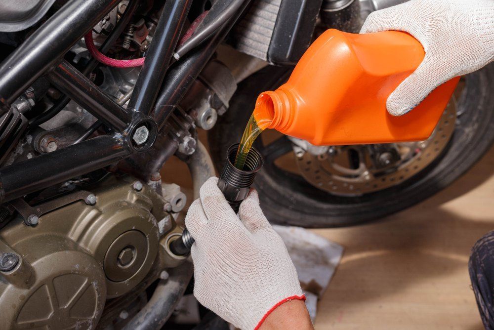 A Person Is Pouring Oil Into a Motorcycle Engine — Fletcher's Truck and 4WD Repair Centre in Hallidays Point, NSW