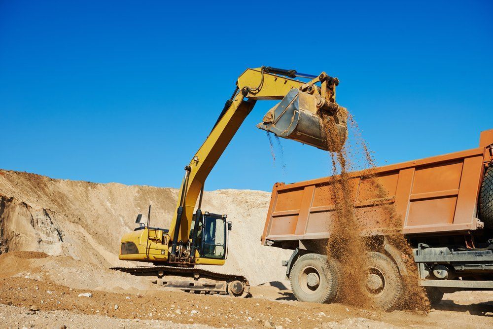 A Yellow Excavator Is Loading Dirt Into a Dump Truck — Fletcher's Truck and 4WD Repair Centre in Tuncurry, NSW