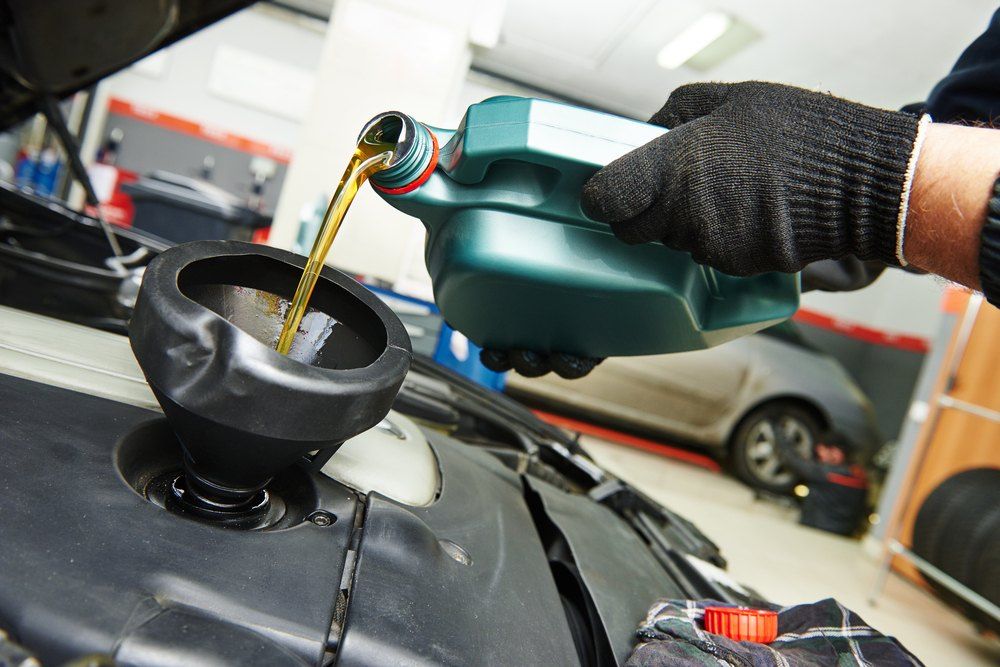 A Person Is Pouring Oil Into a Car Engine — Fletcher's Truck and 4WD Repair Centre in Tuncurry, NSW