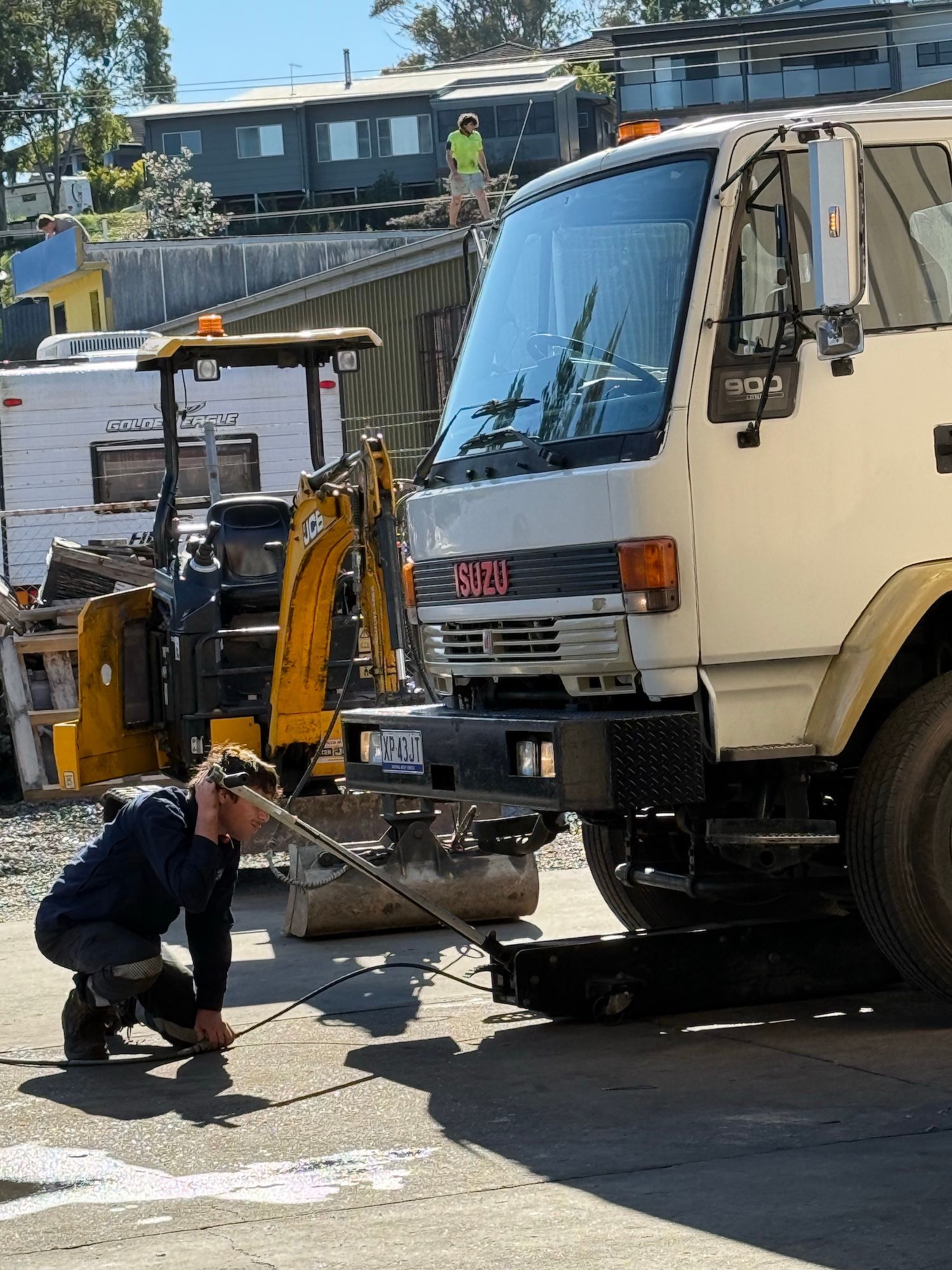 Worker kneels beside a tow truck’s front wheel, repairing or inspecting it on a street.