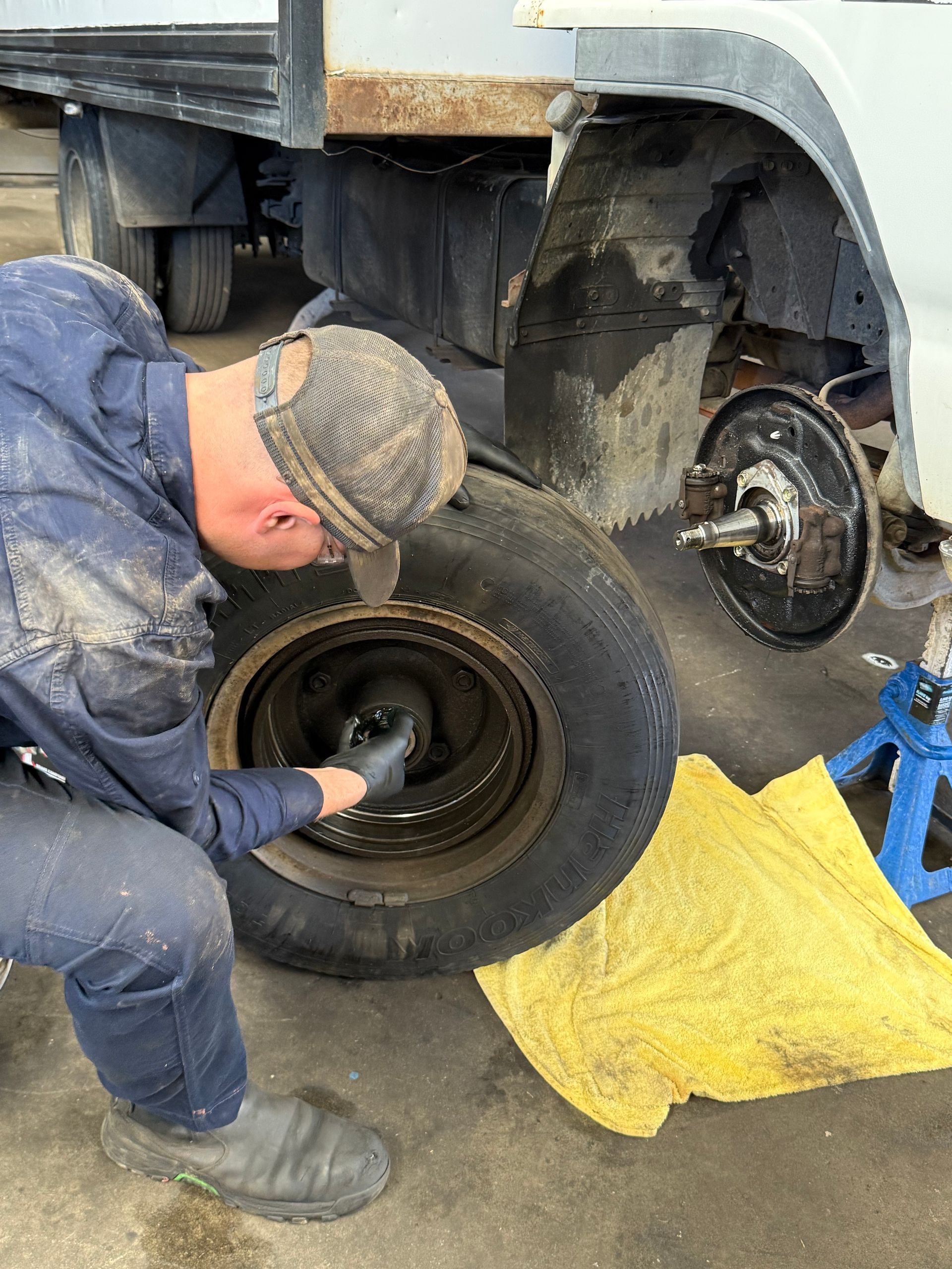 Mechanic kneeling by a truck tire, tightening lug nuts with a wrench beside a yellow mat