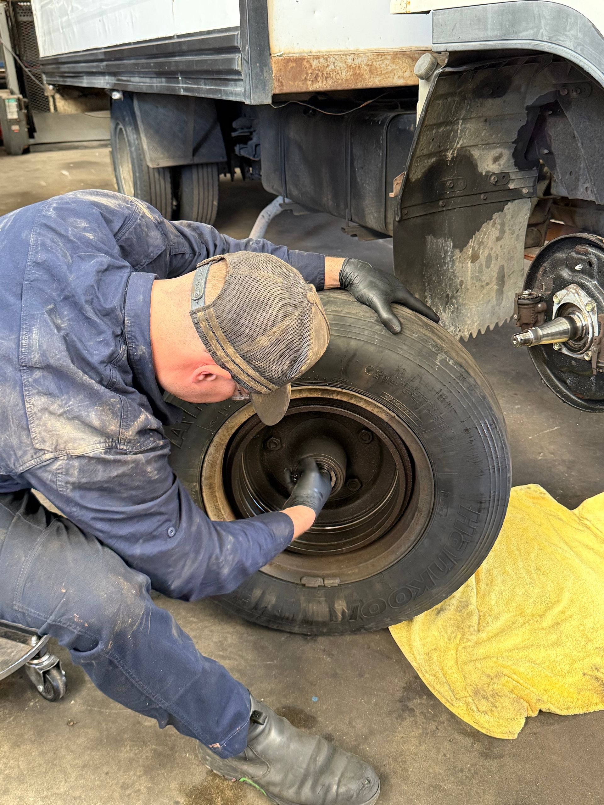 Mechanic removing a truck wheel with a wrench, beside a yellow cloth on the ground.