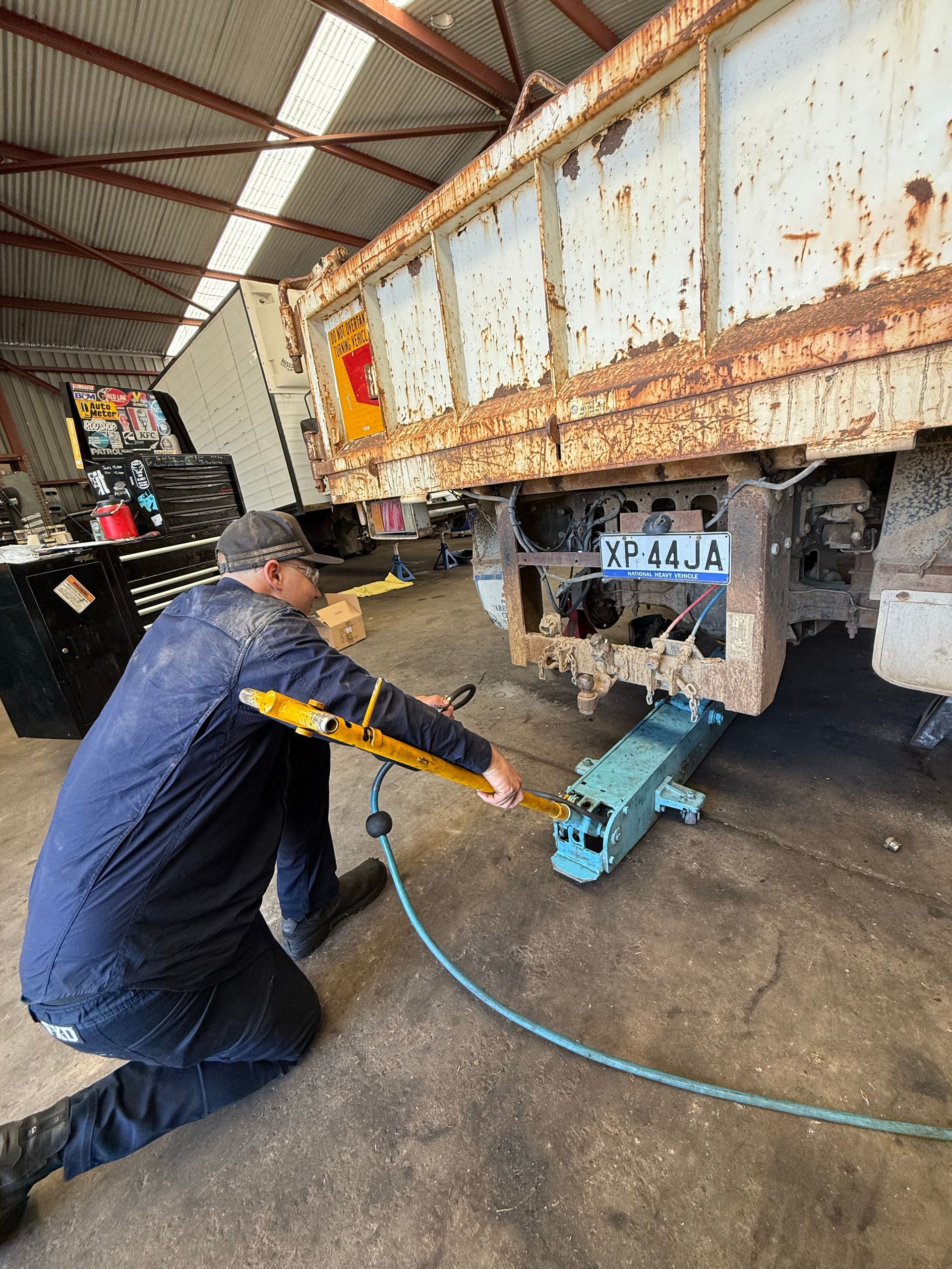 Worker using a blue hydraulic tool on a rusted truck in a warehouse