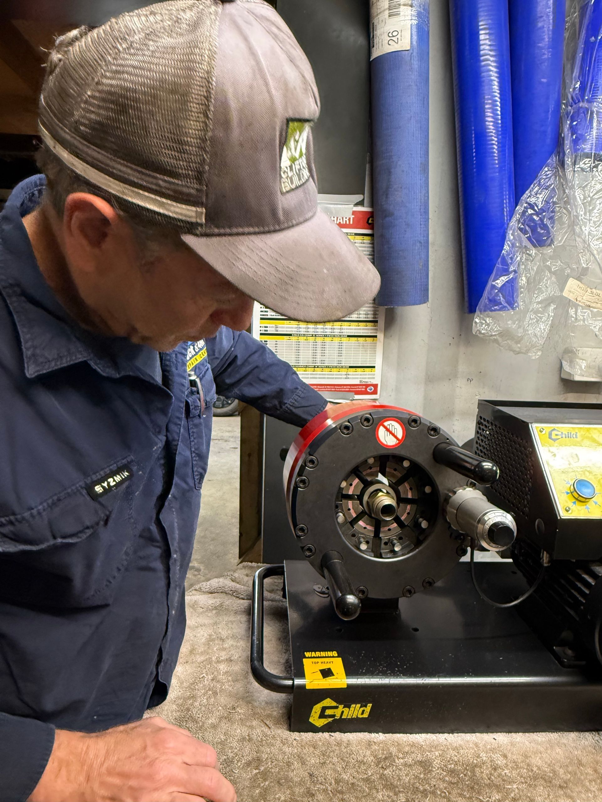 Worker inspecting a metal machine on a workbench in a shop, with blue hoses hanging behind.