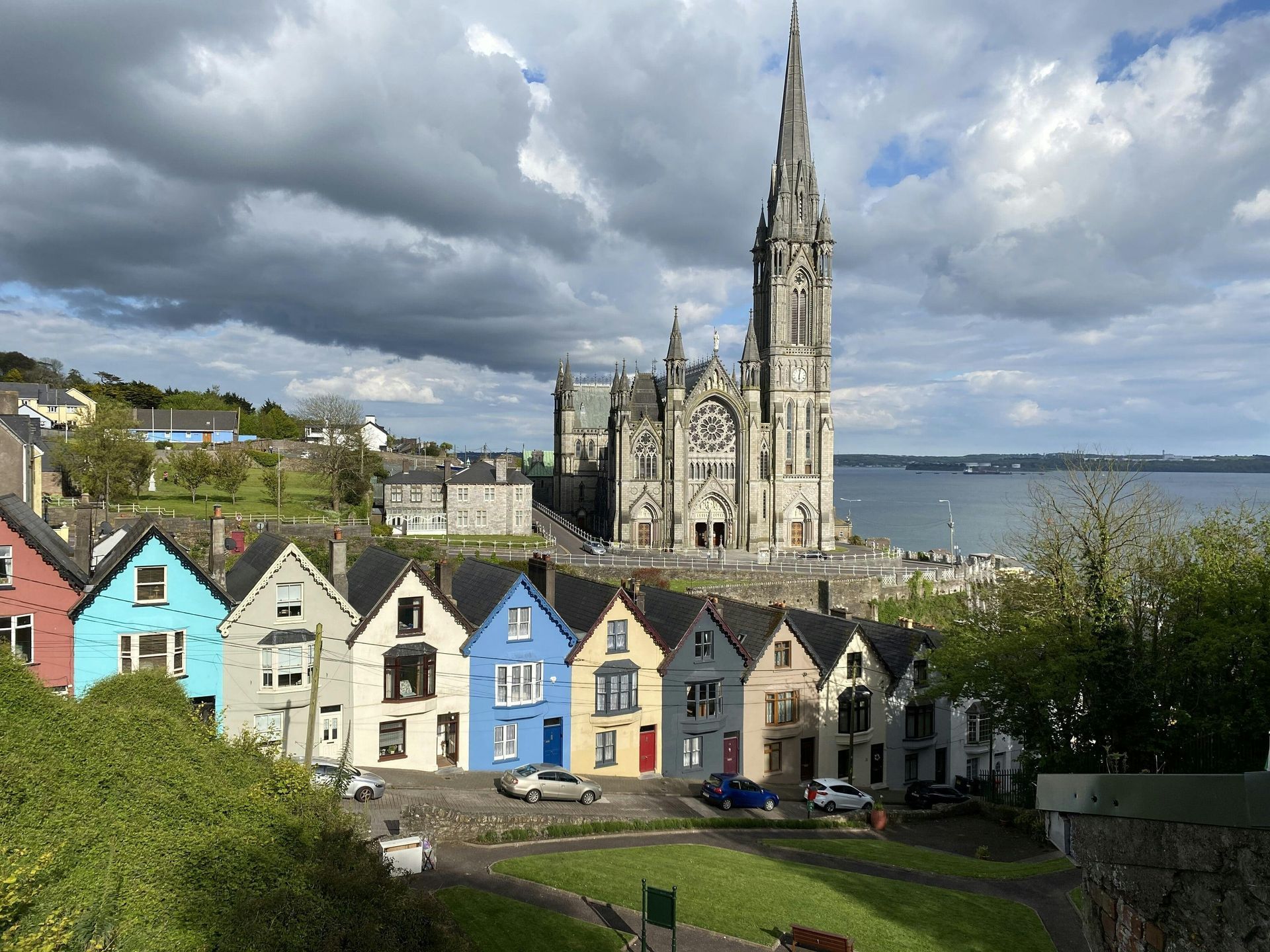 Färgglada hus under en hög katedral i Cobh, Irland, med utsikt över vattnet.