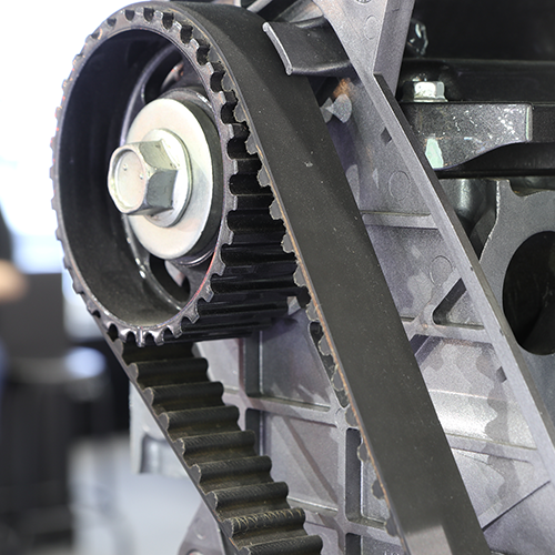Close-up of a black timing belt and pulleys on a gray engine block.