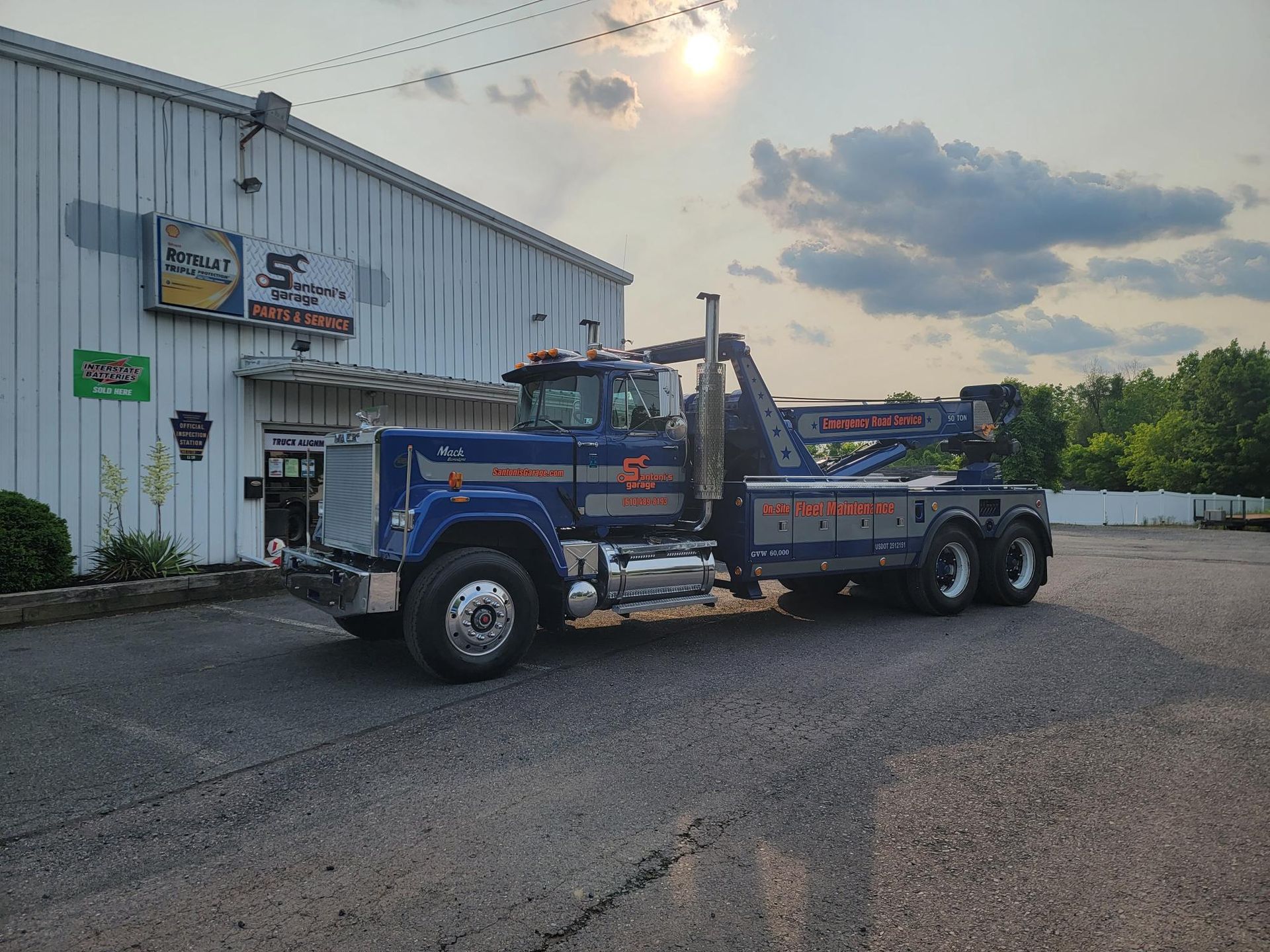 Blue tow truck parked in front of a building; sun overhead.
