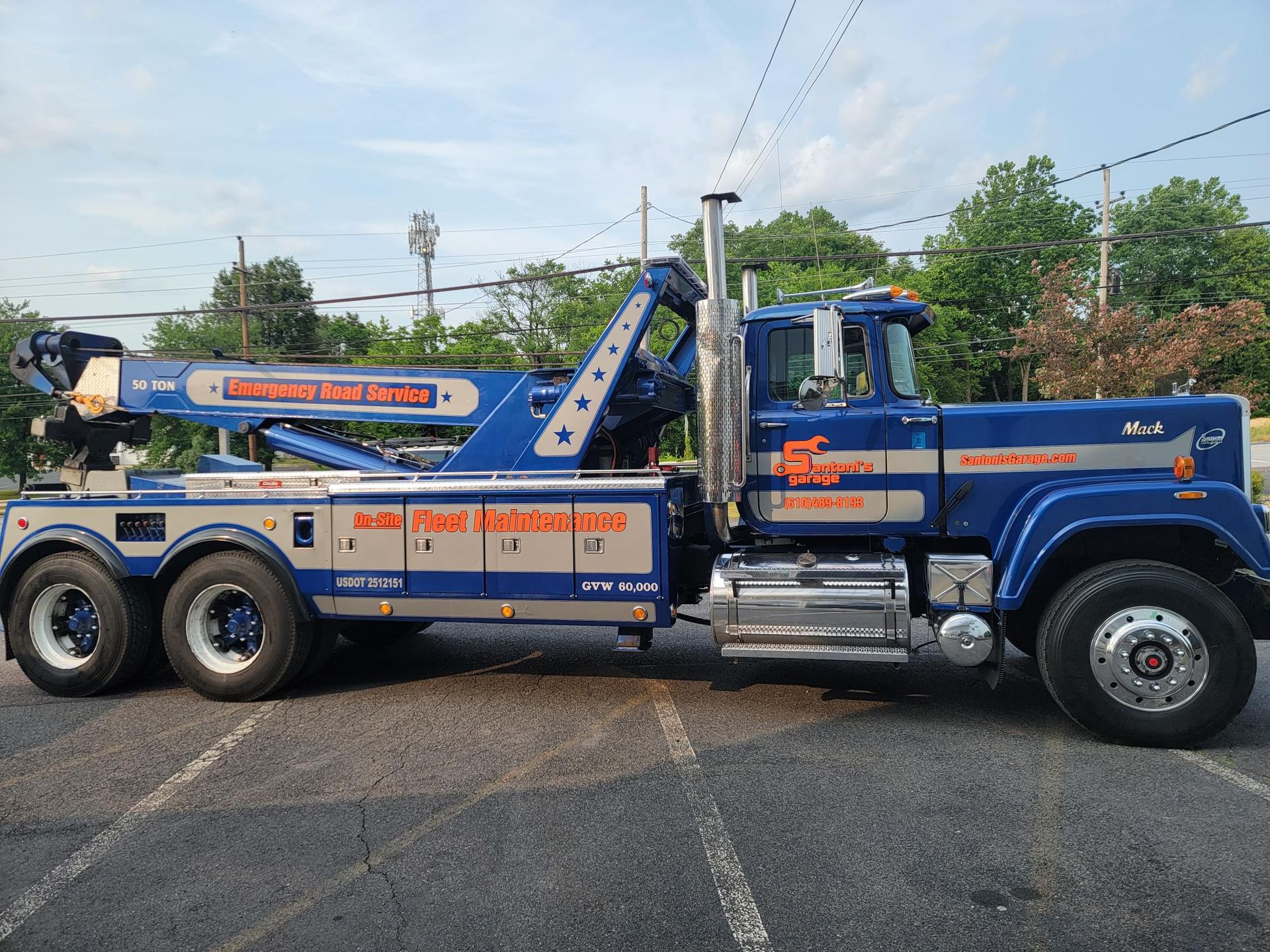 Blue and silver tow truck on asphalt; parked, boom extended, clear sky.