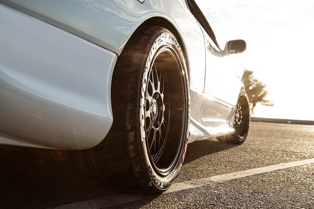 White car with black rims on asphalt, sunlit.