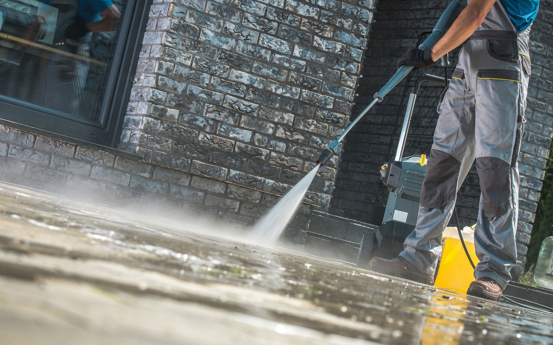 A man is using a high pressure washer to clean a driveway.