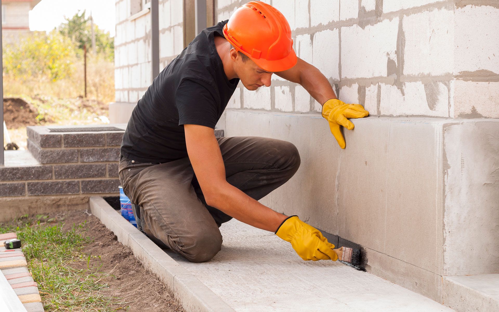 A man wearing a hard hat is kneeling down and painting a sidewalk.