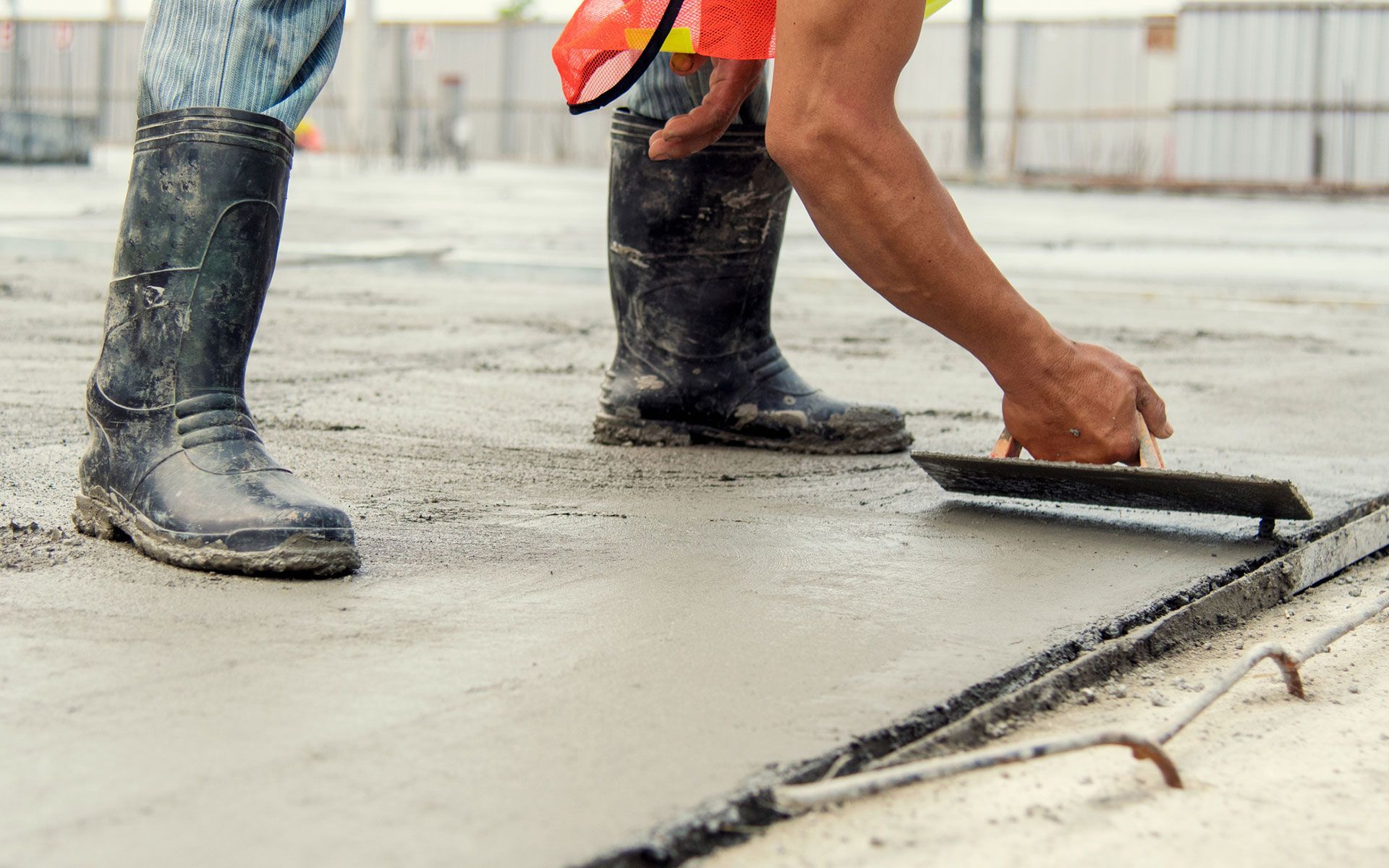 A construction worker is spreading concrete on the ground with a trowel.