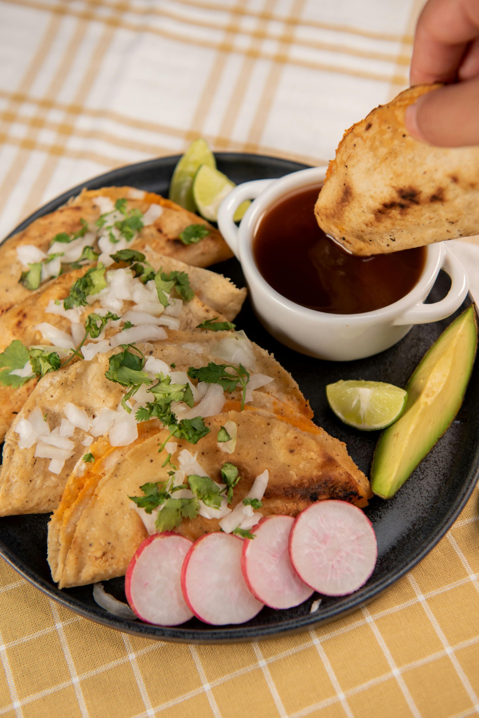 A person is dipping a taco into a bowl of sauce.
