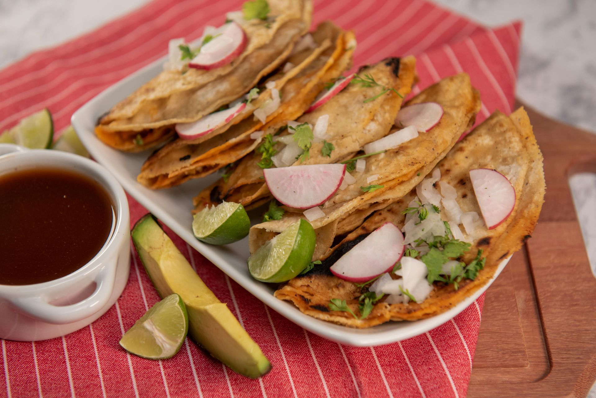 A white plate topped with tacos , radishes , onions and limes.