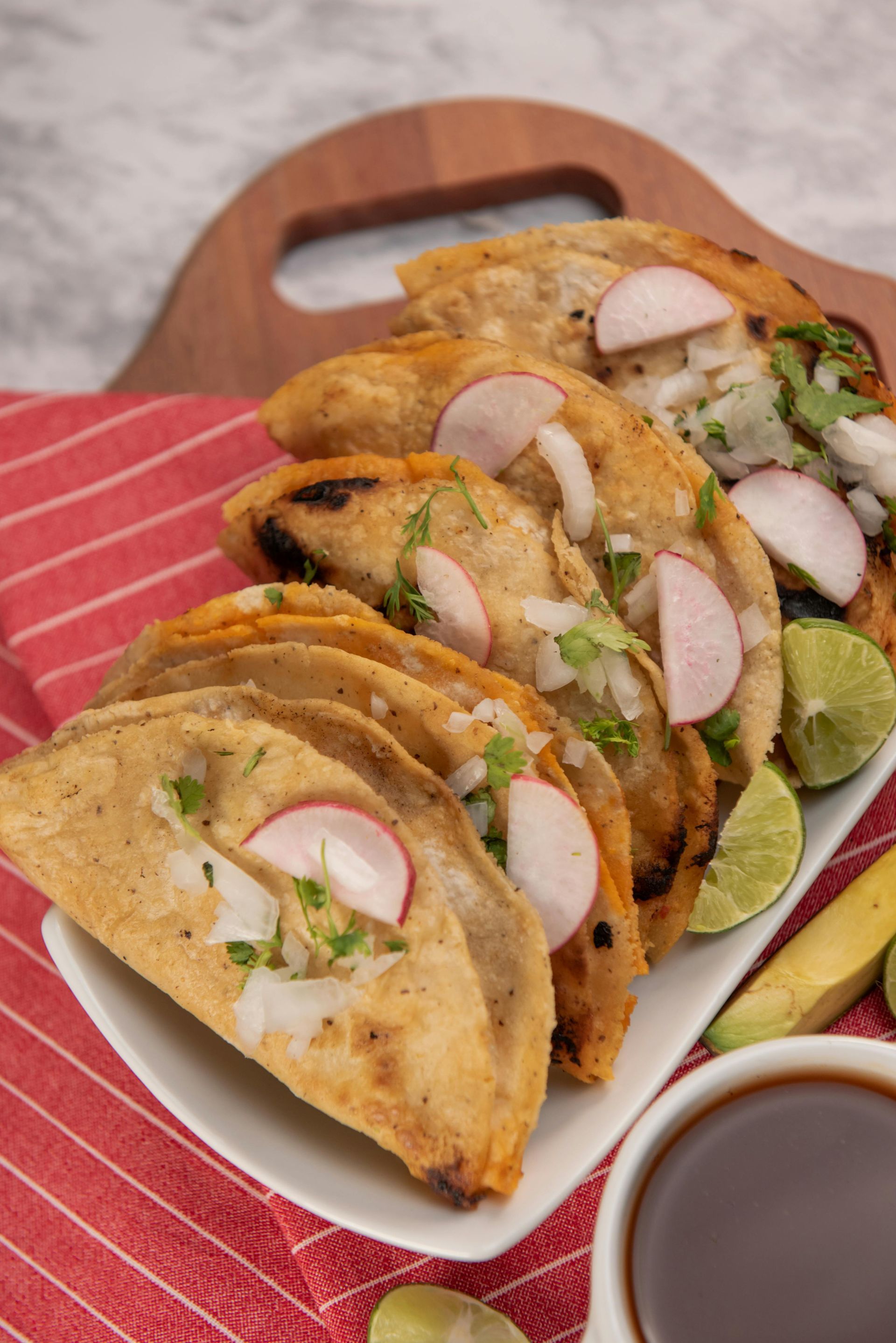 A white plate topped with tacos and radishes next to a cup of coffee.