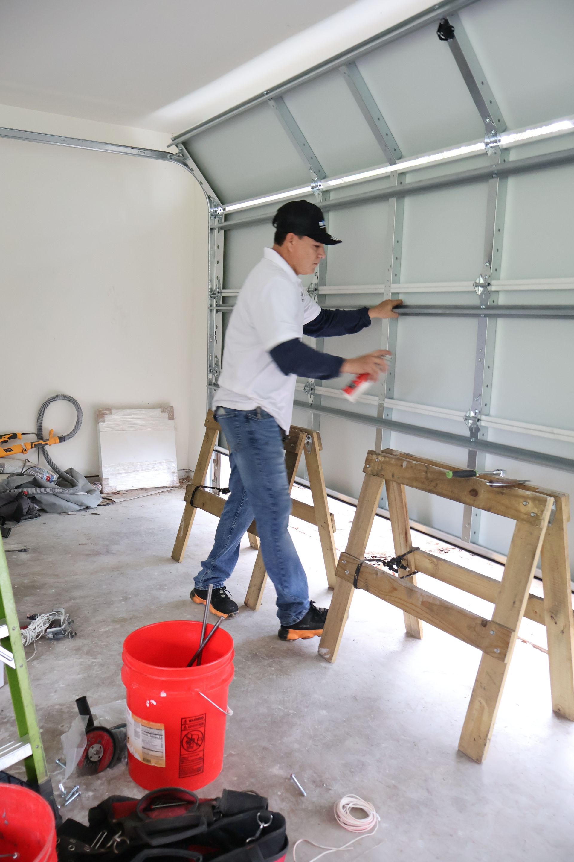 Worker painting a garage door interior with a red bucket and tools nearby