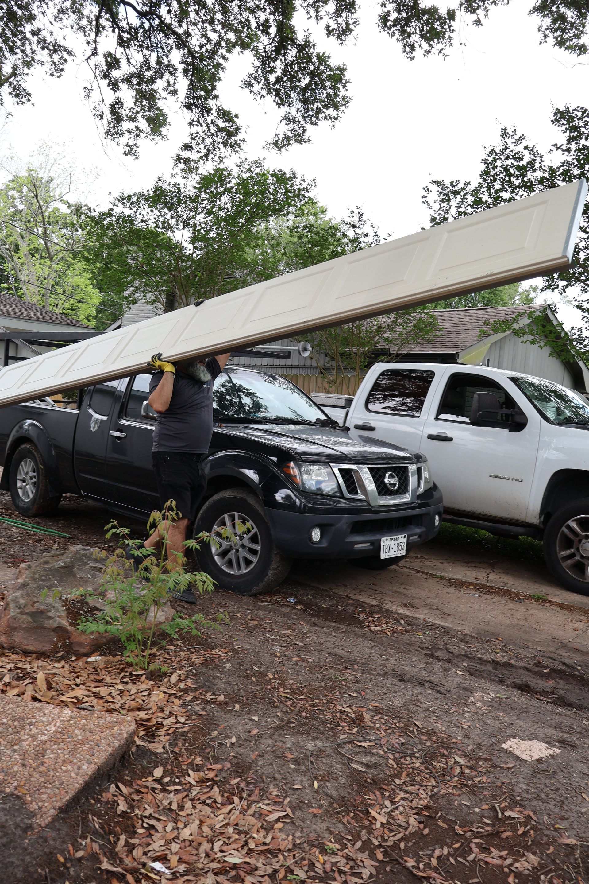 Workers lifting a long white beam onto parked trucks in a wooded area